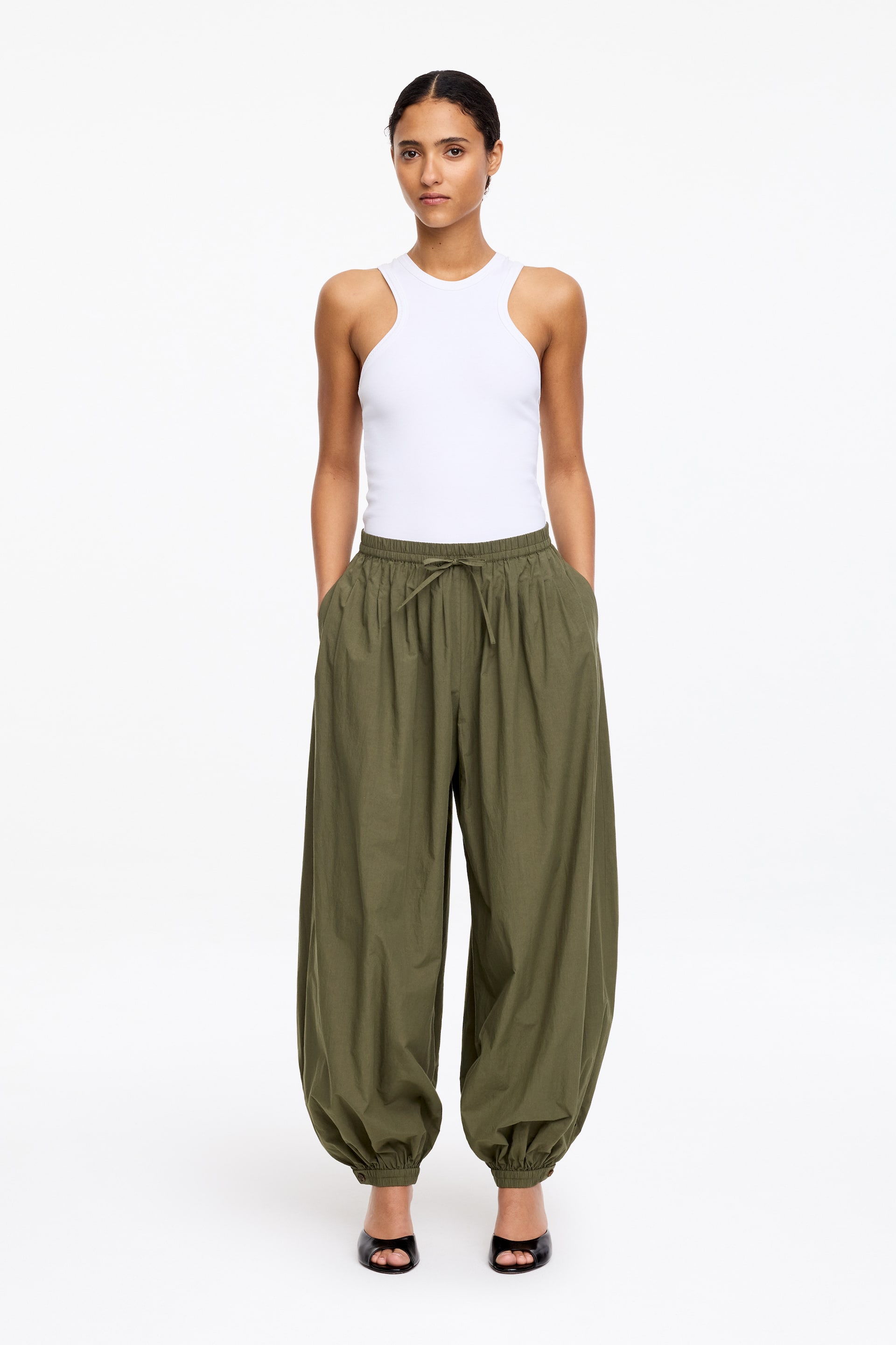 View larger image: Olive green wide-leg trousers feature an elasticated drawstring waist, side pockets, and gathered elasticated cuffs. The trousers present a voluminous, relaxed fit from the front.