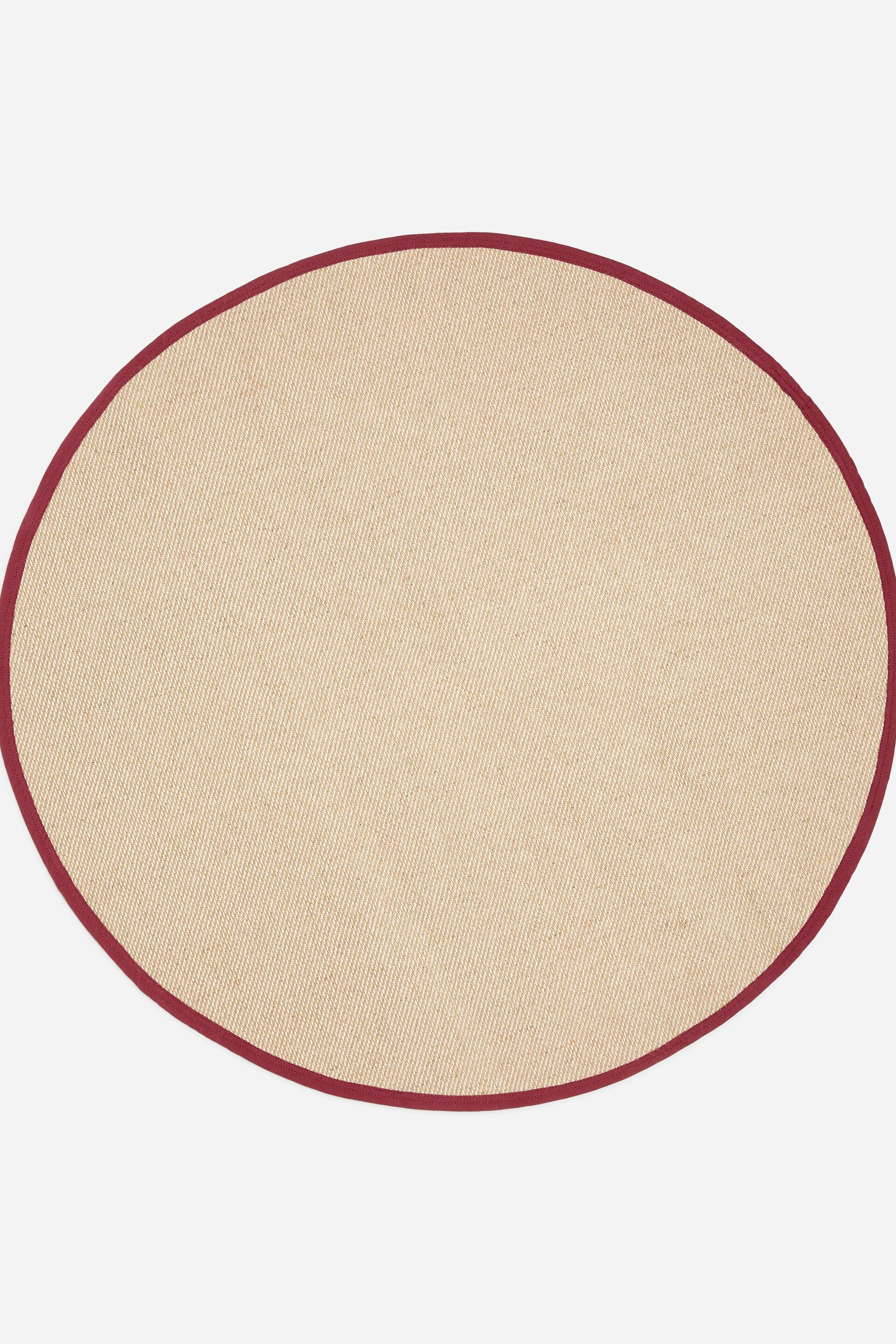View larger image: A round rug made from a woven beige jute-cotton blend lies flat, showcasing its circular shape and contrasting dark red fabric trim around the outer edge.
