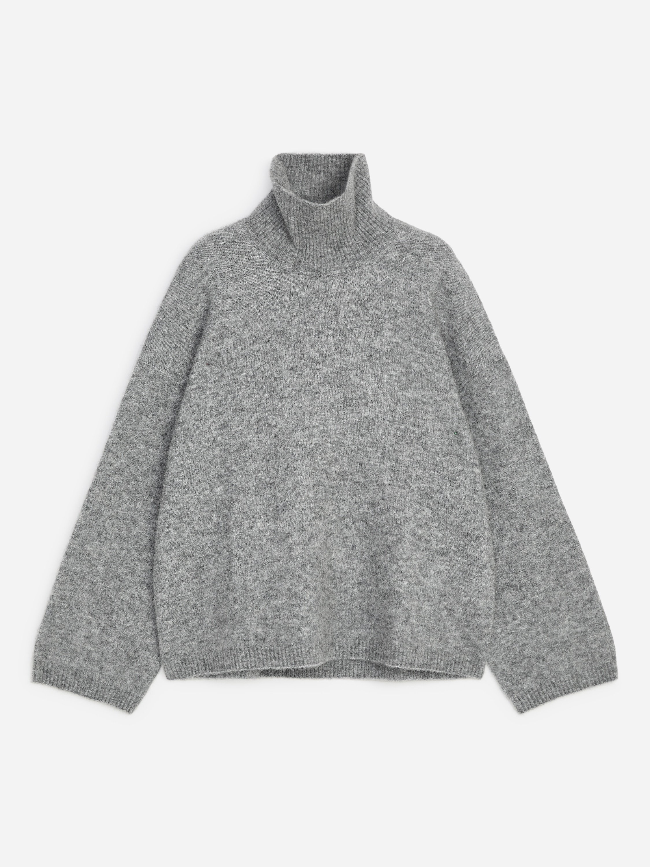 Ein grauer Rollkragenpullover mit flauschiger Struktur, Oversize-Silhouette und RippbÃ¼ndchen wird vom Model getragen. Das Model kombiniert das Strickteil mit dunklen, weit geschnittenen Hosen.