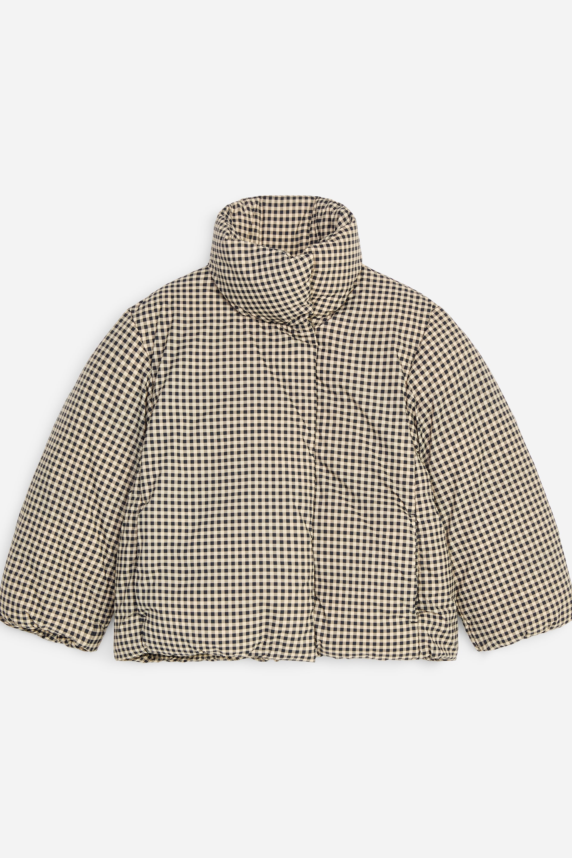 Grotere afbeelding bekijken: Een pufferjas met een zwart-beige ginghampatroon wordt van voren getoond en laat het gewatteerde ontwerp en de hoge, opstaande funnelkraag zien. De jas heeft lange, wijde mouwen en een verborgen sluiting aan de voorkant met een gerimpelde zoom.