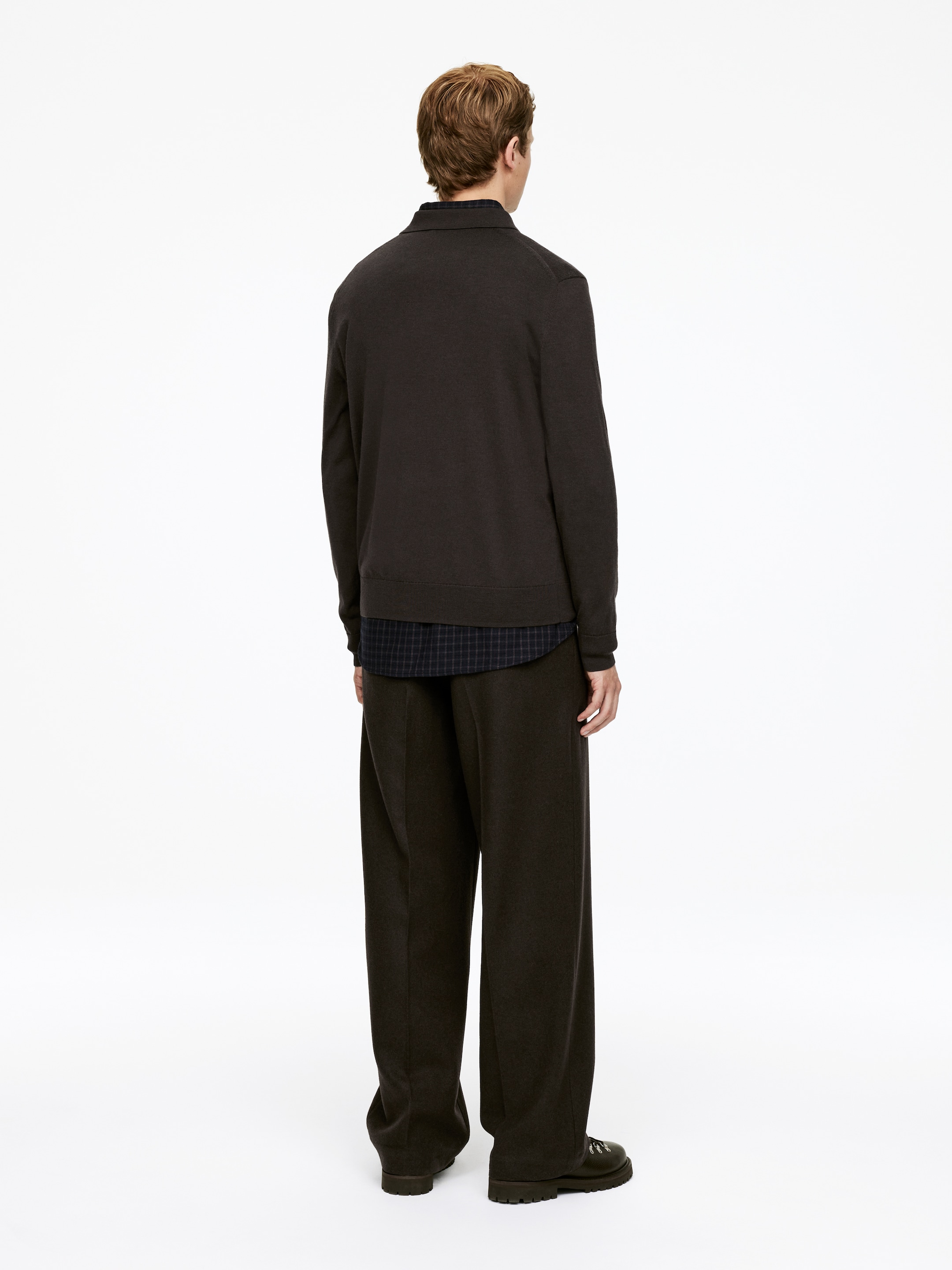 Agrandir l'image: Un haut à col tricoté brun foncé est présenté de dos, superposé à une chemise à carreaux foncés. Il est assorti à un pantalon large brun foncé.