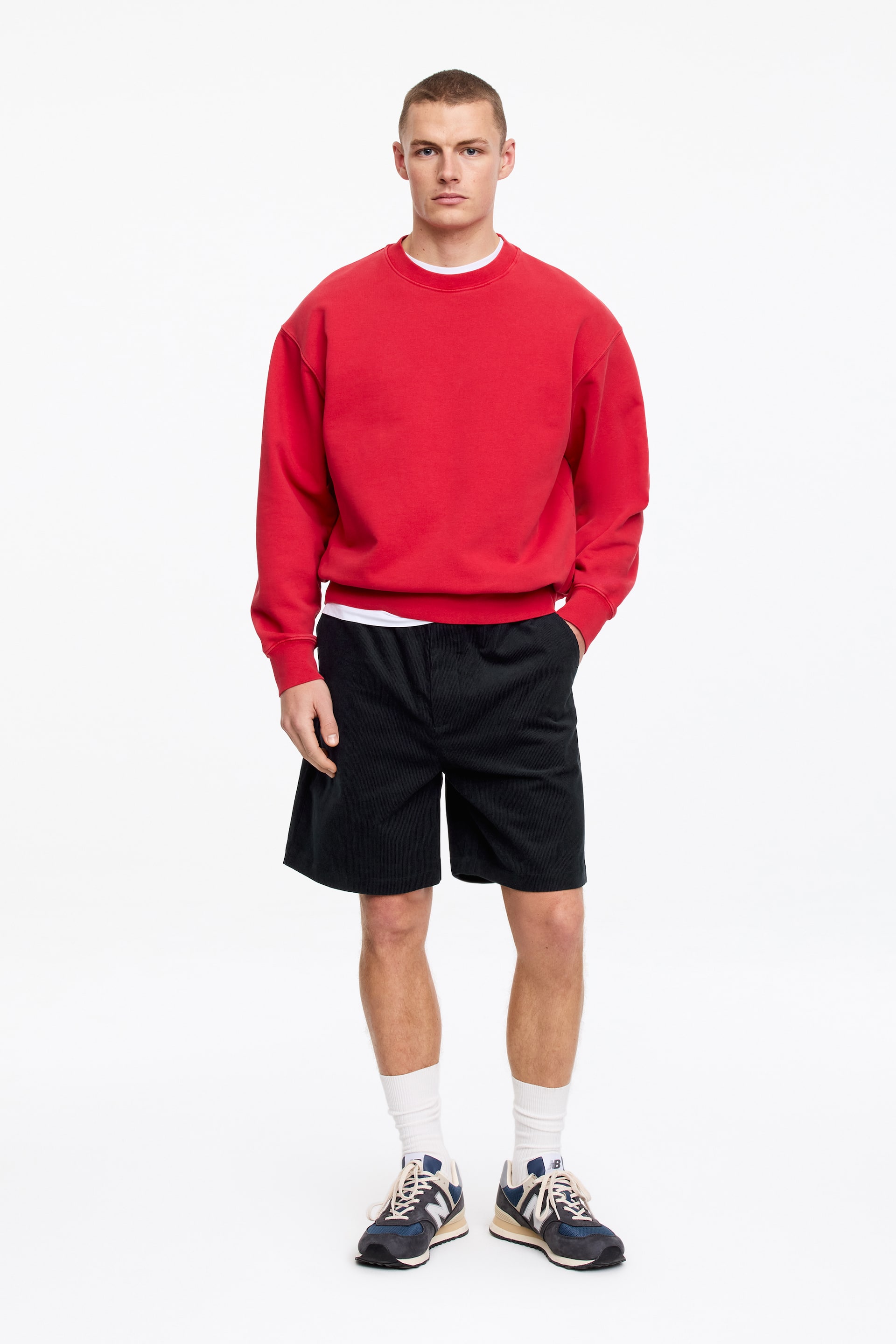 Ver imagem maior: Uma sweatshirt vermelha com decote redondo está a ser apresentada de frente, apresentando um corte descontraído, mangas compridas com punhos canelados e uma bainha canelada, com uma t-shirt branca visivelmente sobreposta por baixo do decote redondo e da bainha.