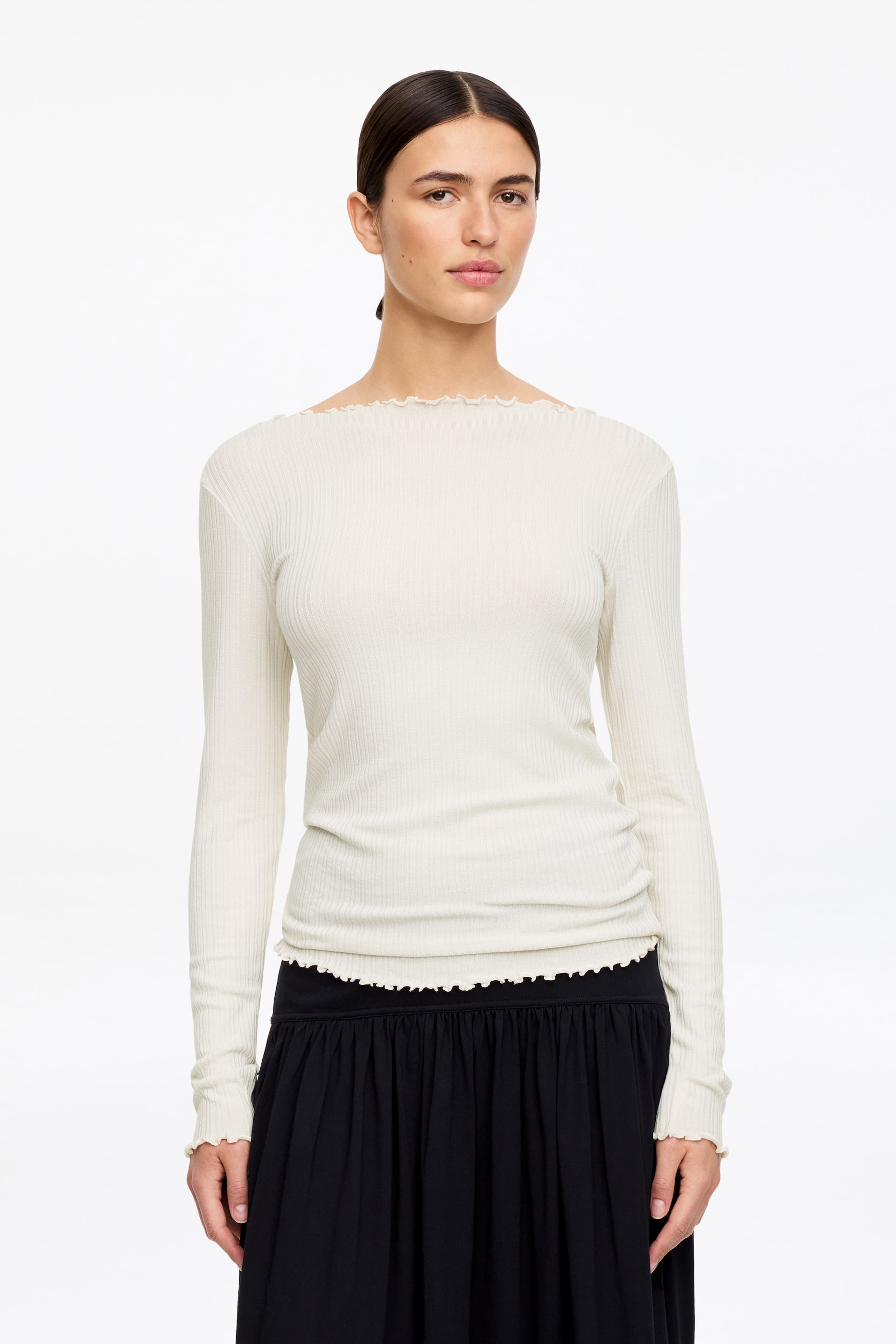 Vis større bilde: En kremfarget ribbestrikket langermet topp vises forfra og har en båthals med rysjekant, tettsittende passform, lange ermer med rysjekanter og en rysjet kant nederst.