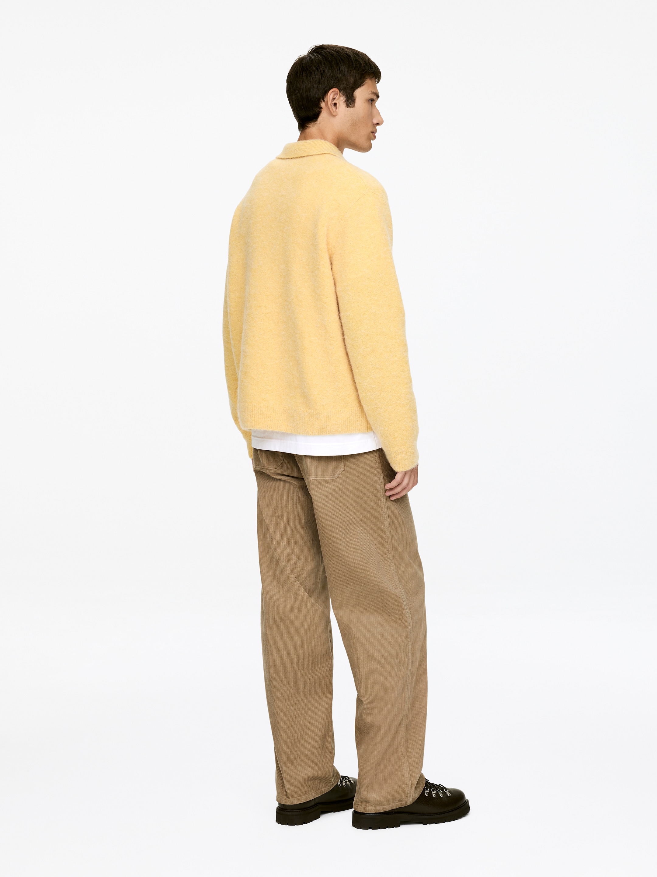 Agrandir l'image: Un pull en tricot flou jaune est présenté de dos et de côté, avec un col pointu et des manches longues. Il est superposé à un t-shirt blanc et assorti à un pantalon en velours côtelé marron à larges côtes et des chaussures foncées à semelles épaisses avec œillets en D.