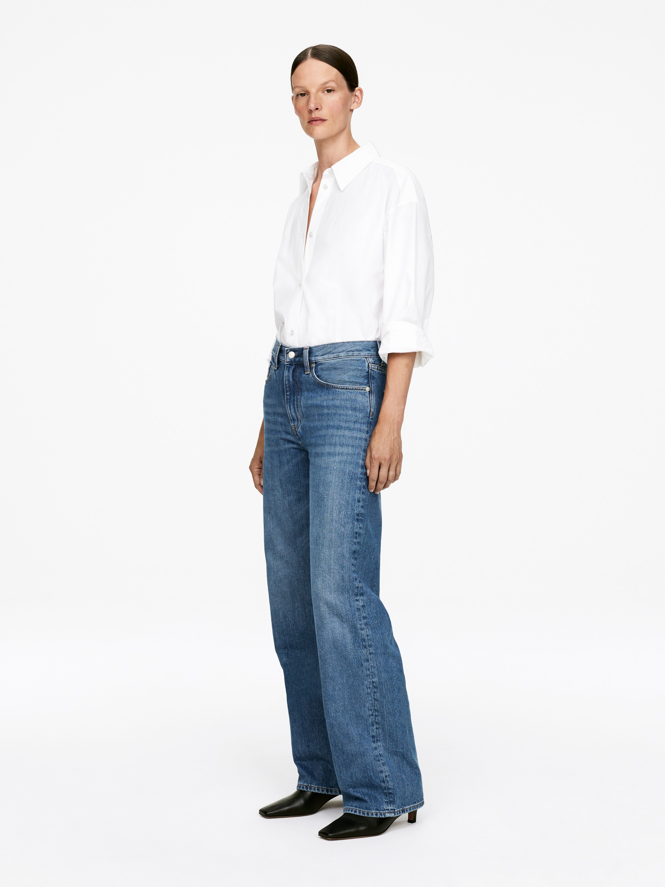 Grotere afbeelding bekijken: Blauwe denim jeans worden vanuit een lichte hoek gepresenteerd, met een hoge taille en een wijde pijp die een ontspannen pasvorm door het been toont. Ze hebben de standaard vijfzakkenstijl en riemlussen.