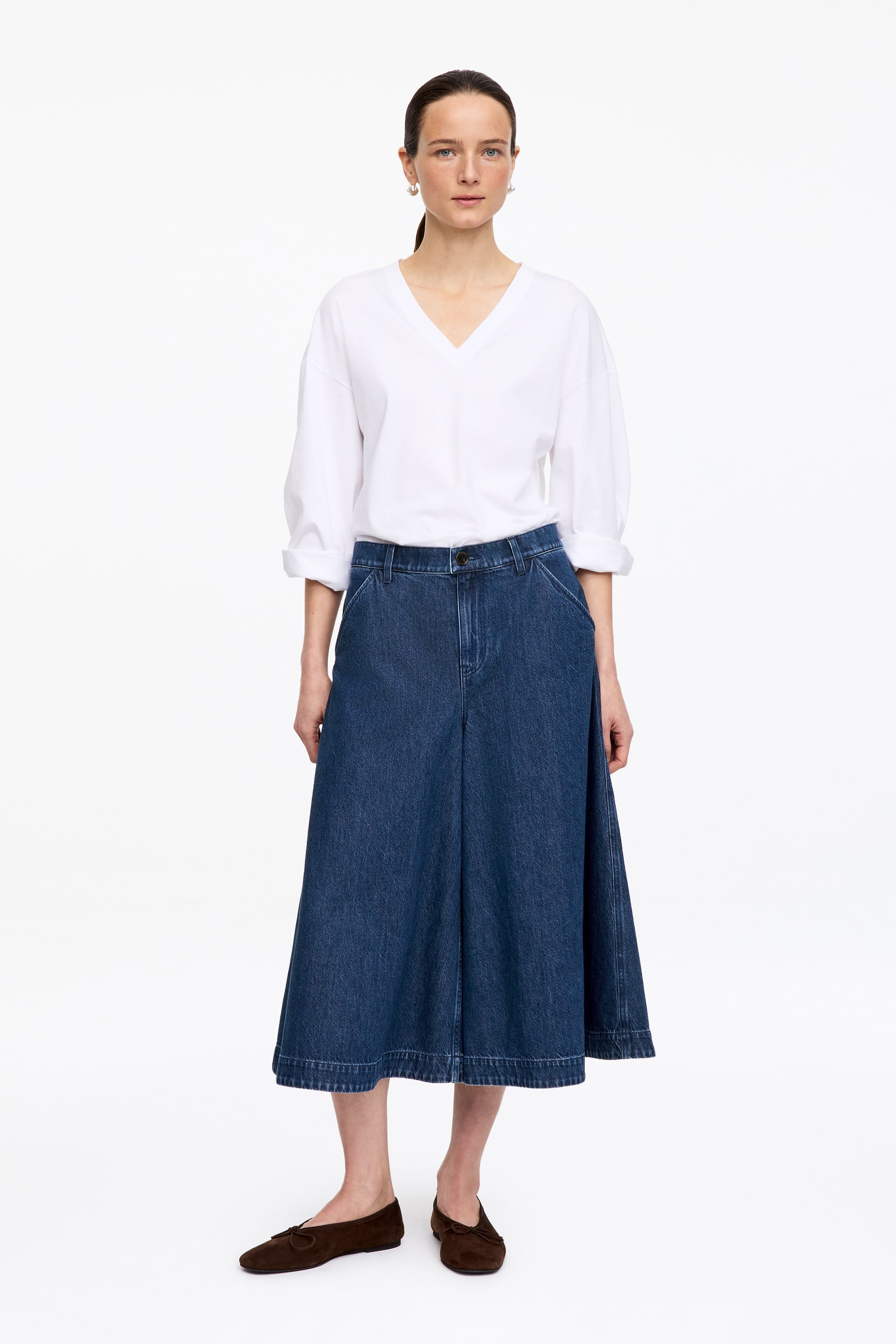 Visa större bild: Mörkblå denim culottes visas framifrån, med en vid benklippning, hög midja med synliga bältesöglor och framfickor, med en beskuren längd som slutar mitt på vaden och en bred sydd fåll.