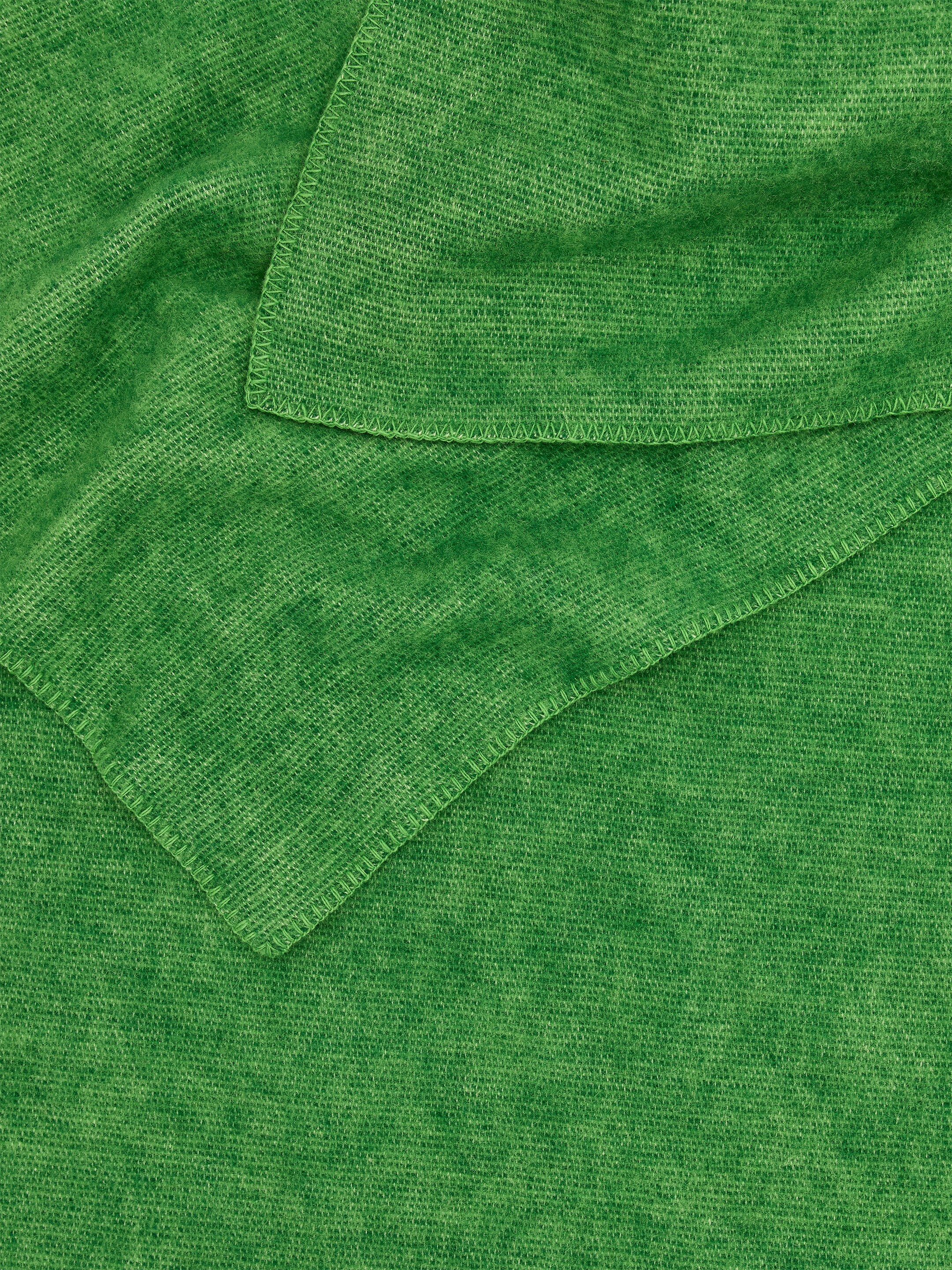 Grotere afbeelding bekijken: Een Klippan wollen deken wordt tentoongesteld, waarbij de groene kleur, de textuur van het weefsel en de dekenstiksel langs de gevouwen randen te zien zijn.