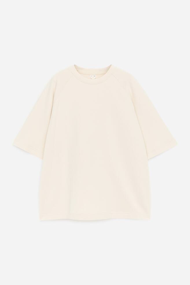 FRENTE. Una camiseta blanca con cuello redondo y ribete acanalado. Presenta mangas cortas raglán y un dobladillo recto. - 1