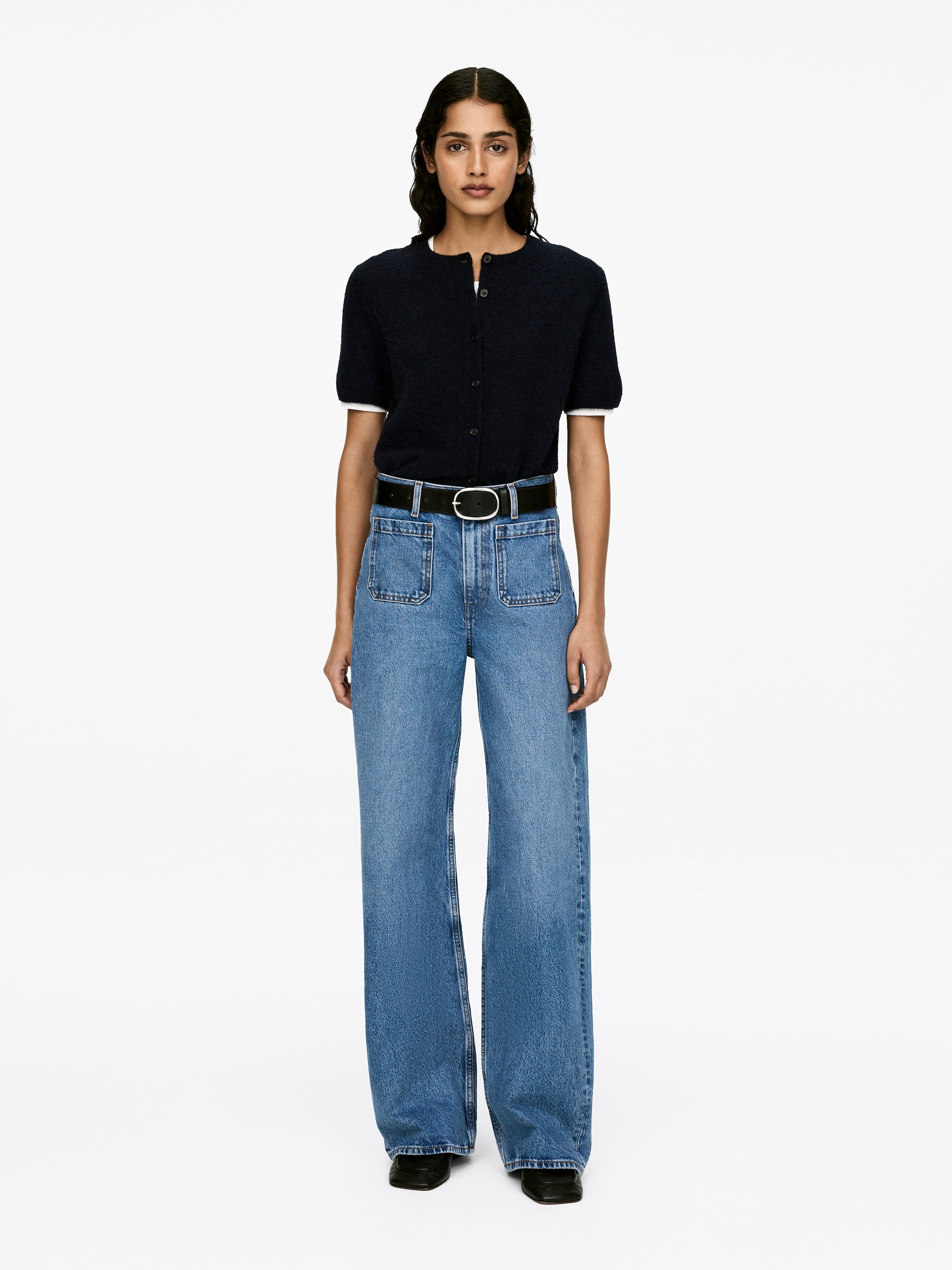 Visa större bild: LUPINE denimjeans bärs av modellen, med hög midja, smal passform och utsvängda ben med synliga främre fickor. Ett svart bälte håller fast jeansens midja, och en mörk kortärmad topp bärs instoppad.