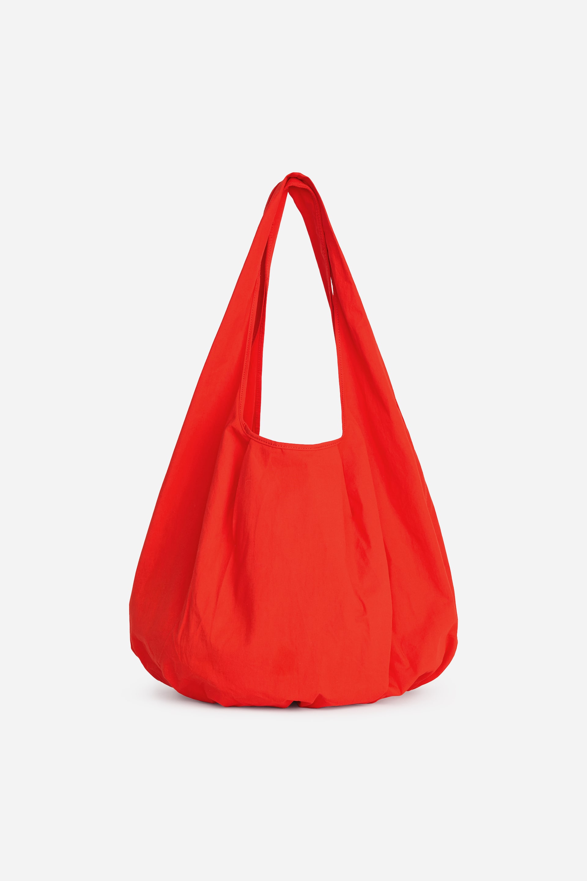 Grotere afbeelding bekijken: Een felrode ronde tote bag staat vooraan, met een zachte, nonchalante body en geïntegreerde stoffen handvatten.