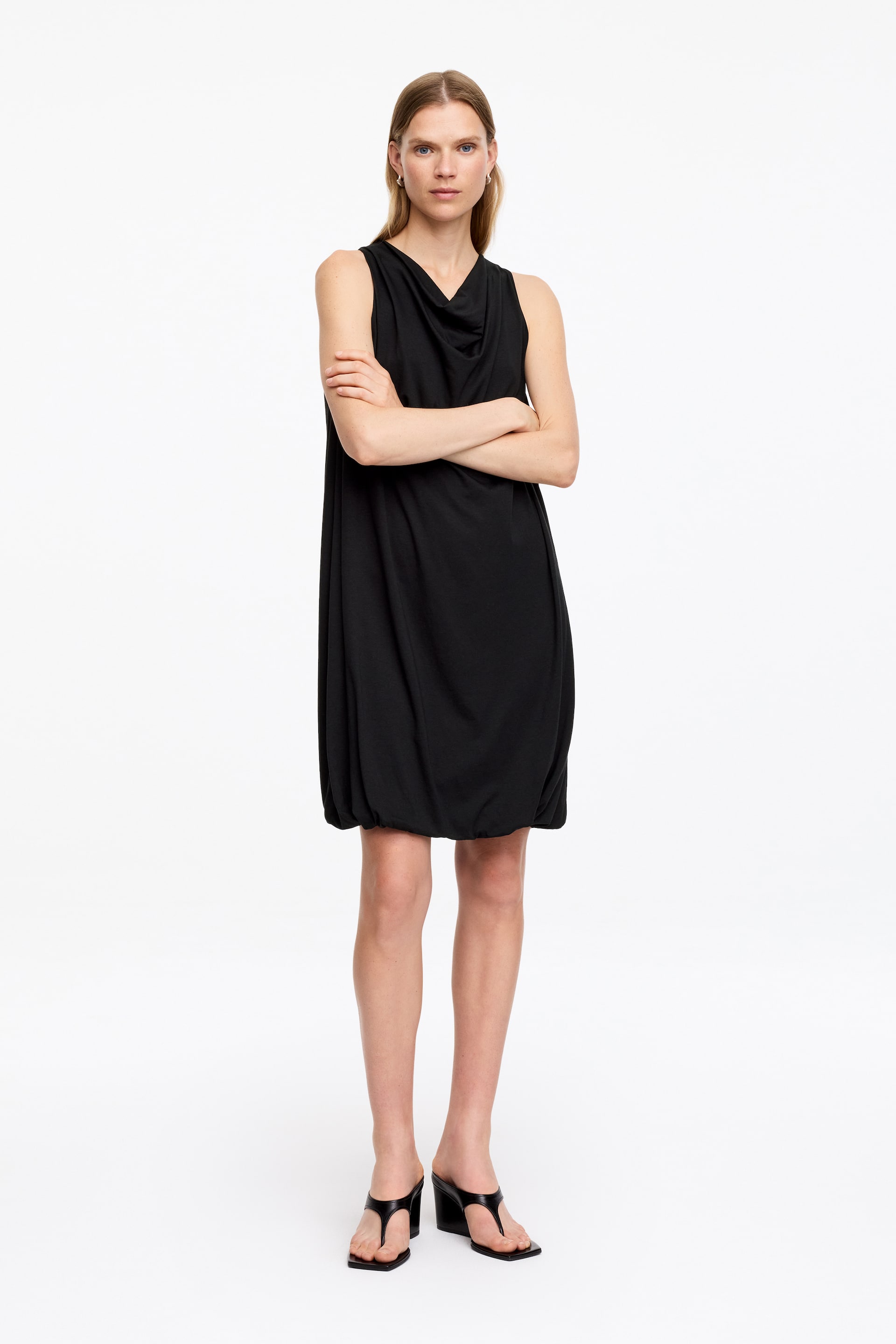 Agrandir l'image: Une robe noire sans manches avec un col bénitier et une coupe décontractée, se resserrant à l'ourlet pour créer une silhouette arrondie.