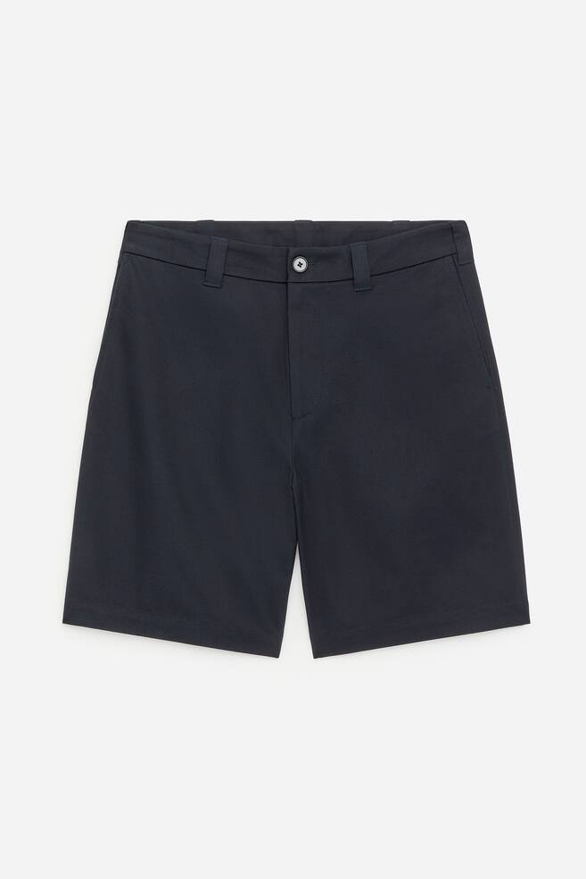 Ein Paar marineblaue Shorts ist von vorne zu sehen, mit einem flachen Bund mit Gürtelschlaufen und einem einzelnen Knopfverschluss, sowie seitlichen Eingrifftaschen und gerade geschnittenen Beinen. - 1