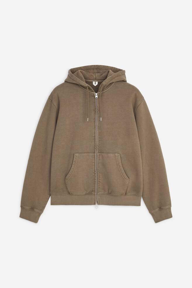 Um hoodie castanho discreto com fecho de correr Ã© apresentado de frente, com capuz com cordÃ£o, fecho frontal prateado e bolso canguru dividido. A peÃ§a Ã© finalizada com punhos canelados e um cÃ³s canelado a condizer. - 1