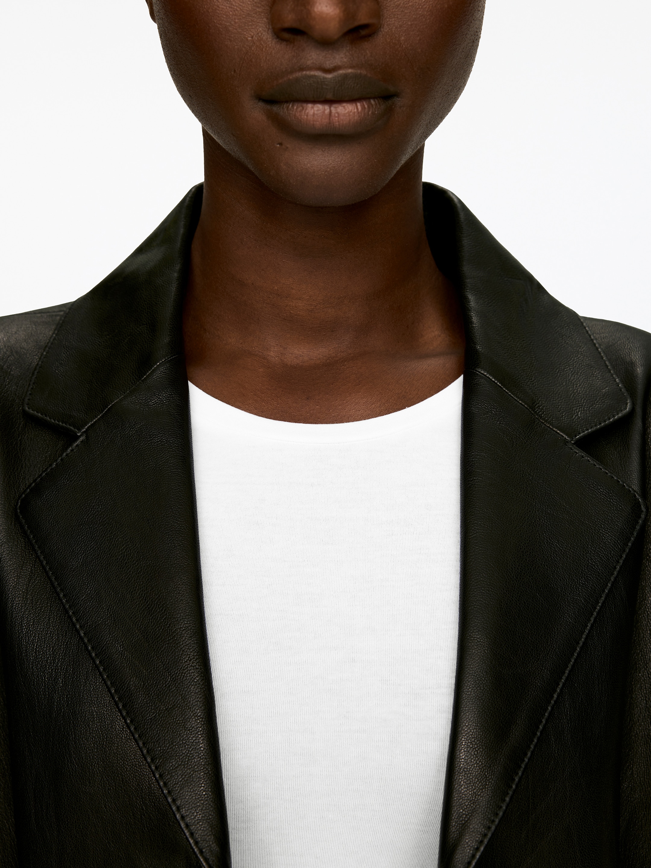 View larger image: A black leather jacket is shown from the front, covering the upper torso. It is featuring wide notch lapels with visible stitching along their edges and is being worn open over a white crew-neck t-shirt.