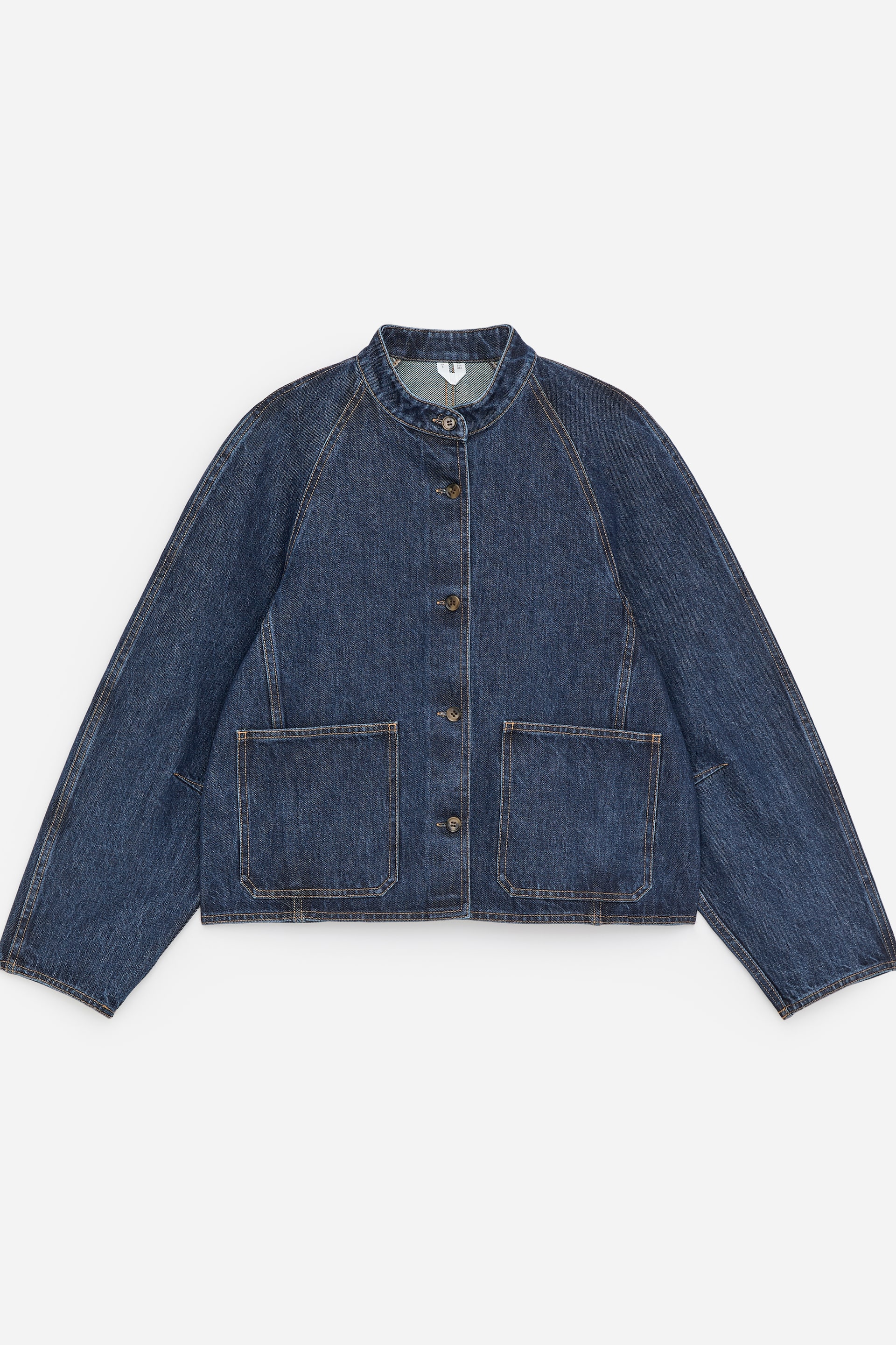 Visualizza l'immagine ingrandita: Una giacca di jeans blu scuro è presentata in vista FRONTALE, caratterizzata da un colletto a fascia e maniche raglan. È progettata con una chiusura frontale a quattro bottoni, due grandi tasche applicate e cuciture a contrasto visibili su tutta la superficie.