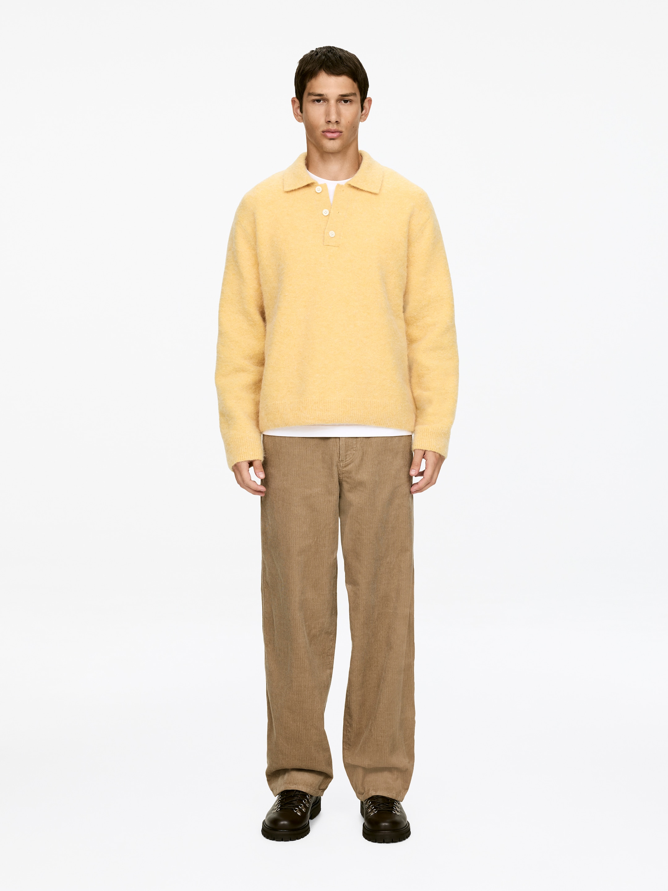 Agrandir l'image: Le modèle porte un pantalon en velours côtelé marron. Ils présentent une coupe décontractée et une jambe plus large, avec des poches avant visibles.