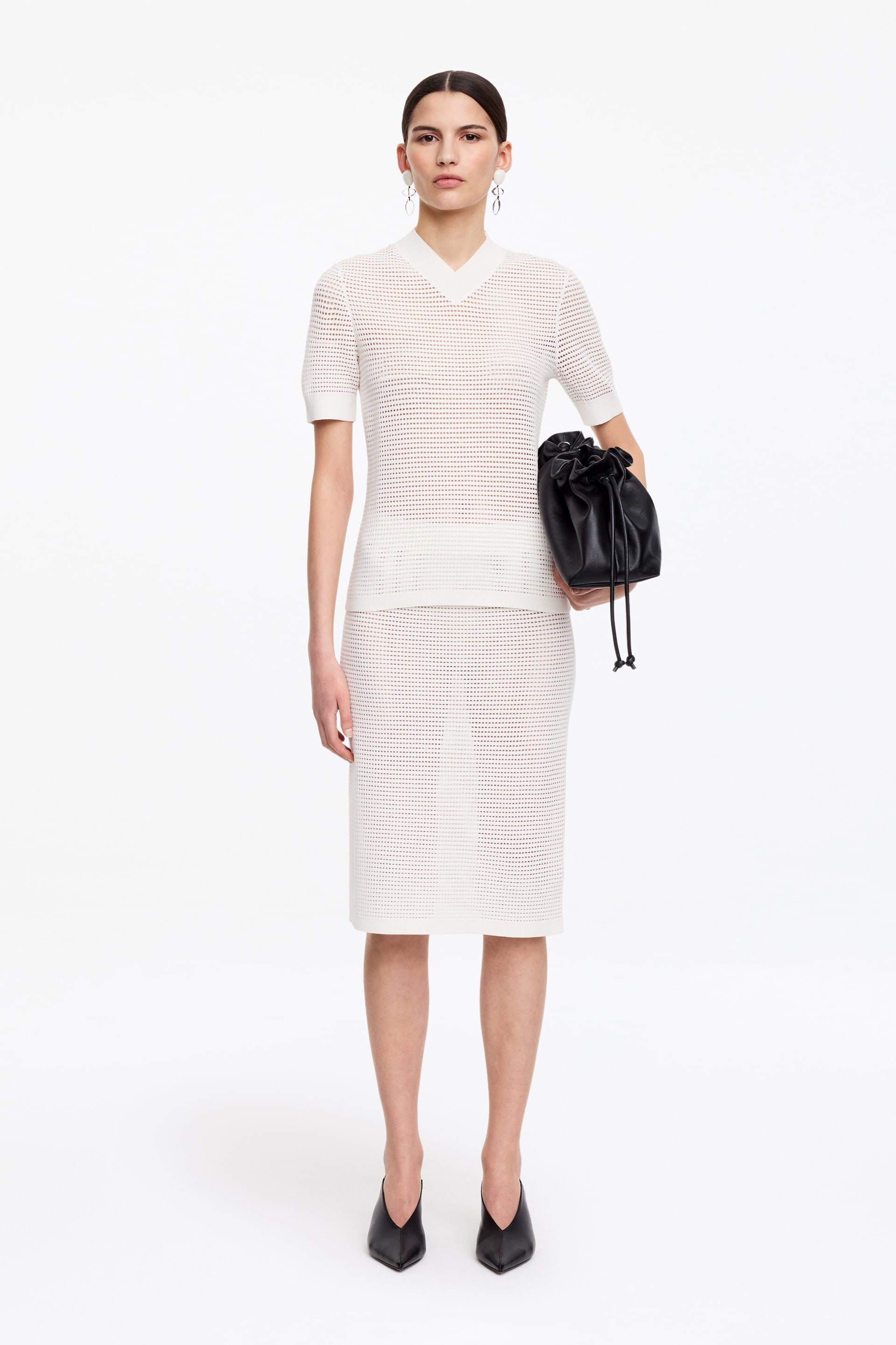 Visa större bild: En vit stickad kortärmad topp och matchande knälång kjol är vända framåt och visar ett genomgående hålmönster. Toppen har en V-ringning och ribbade muddar på de korta ärmarna och fållen, medan den raka kjolen når precis nedanför knät.