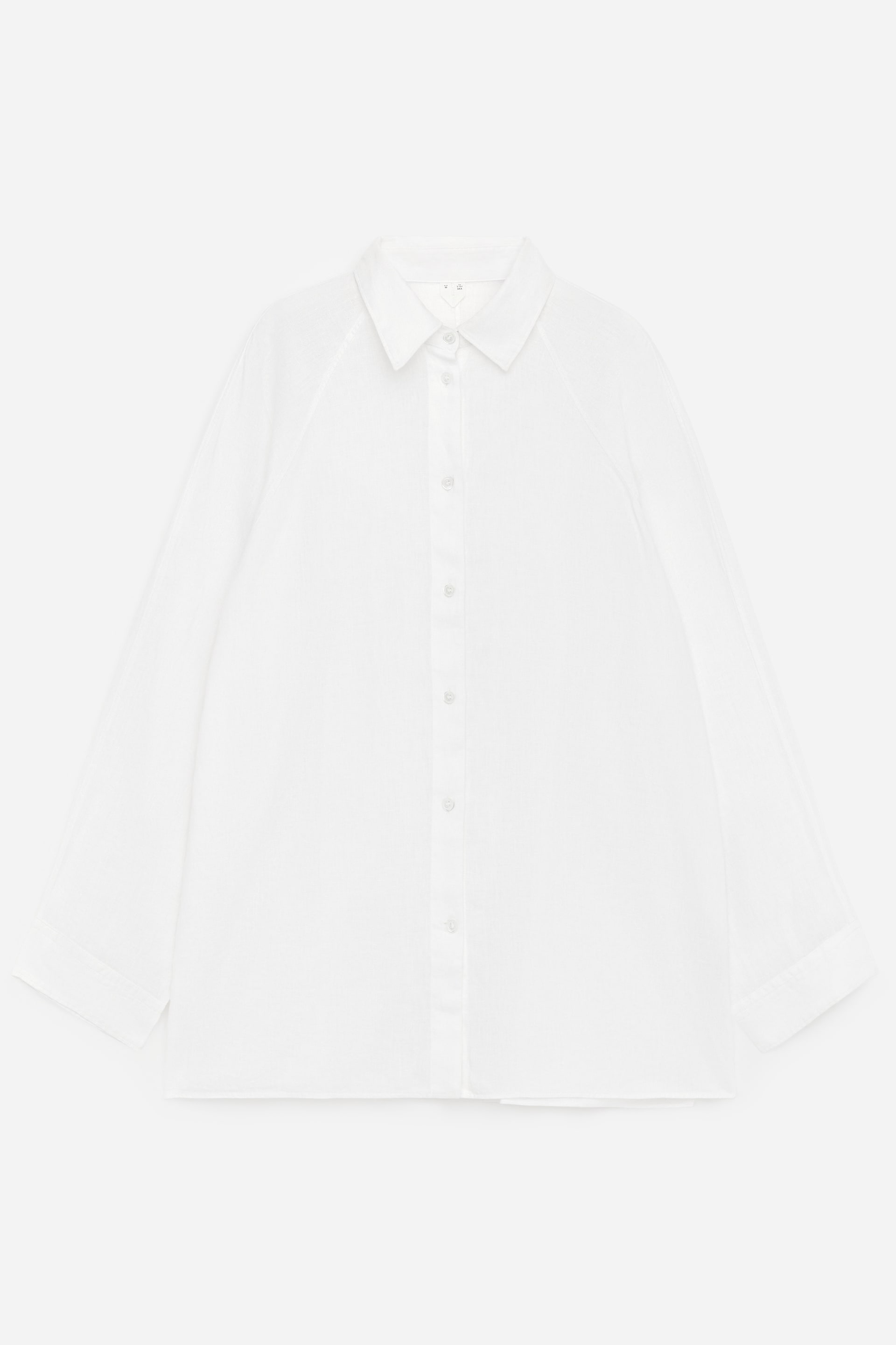 Visualizza immagine più grande: Una camicia bianca è presentata nella sua vista FRONTALE, caratterizzata da un colletto a punta e una chiusura con bottoni a tutta lunghezza con bottoni bianchi. Presenta maniche lunghe e ampie con cuciture raglan e polsini semplici, e una sottile texture verticale è visibile nel tessuto.