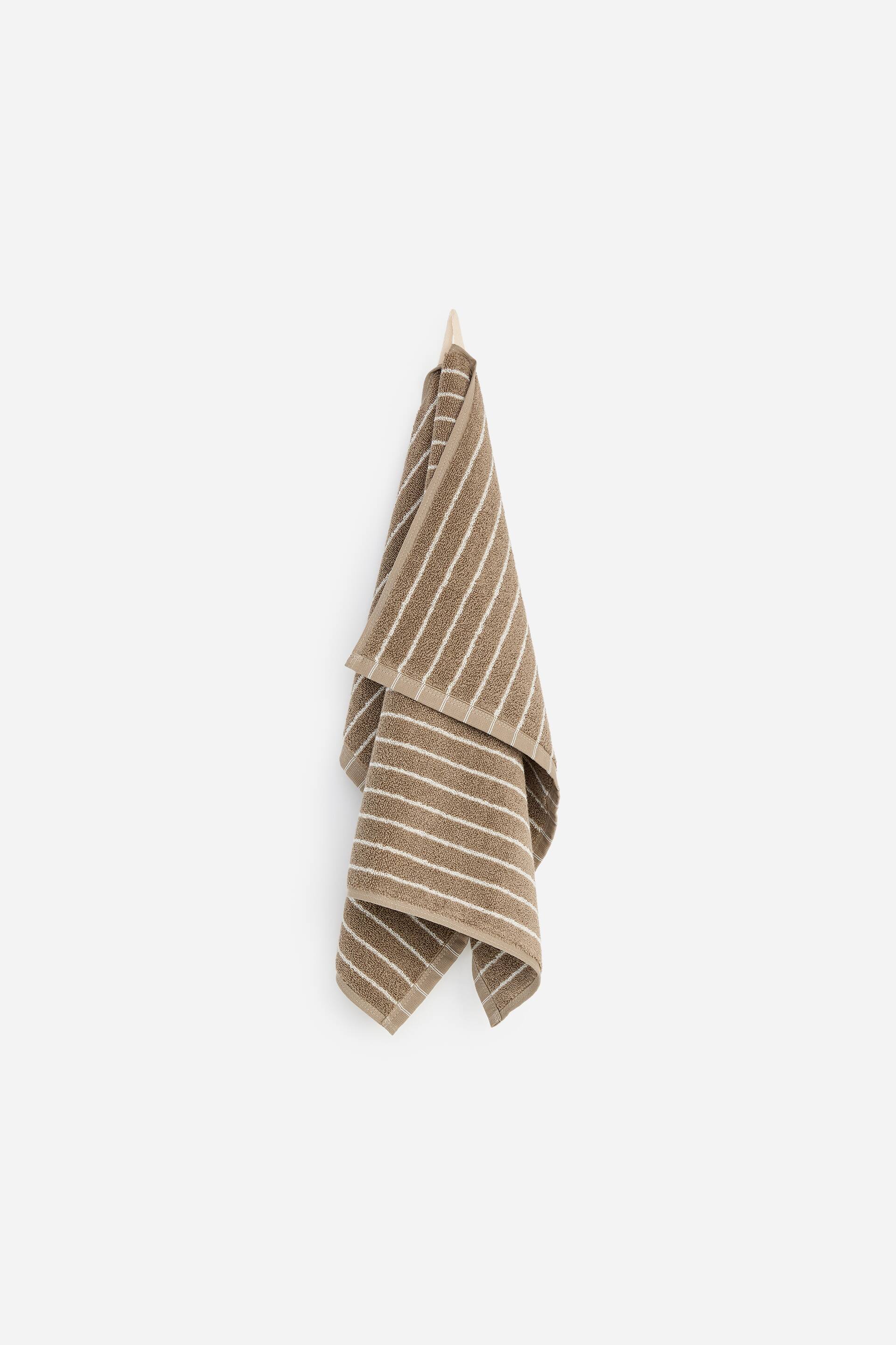 Agrandir l'image: Une serviette à main, en tissu éponge marron avec des rayures horizontales blanches, est suspendue par sa boucle à un crochet, présentant son côté avant.