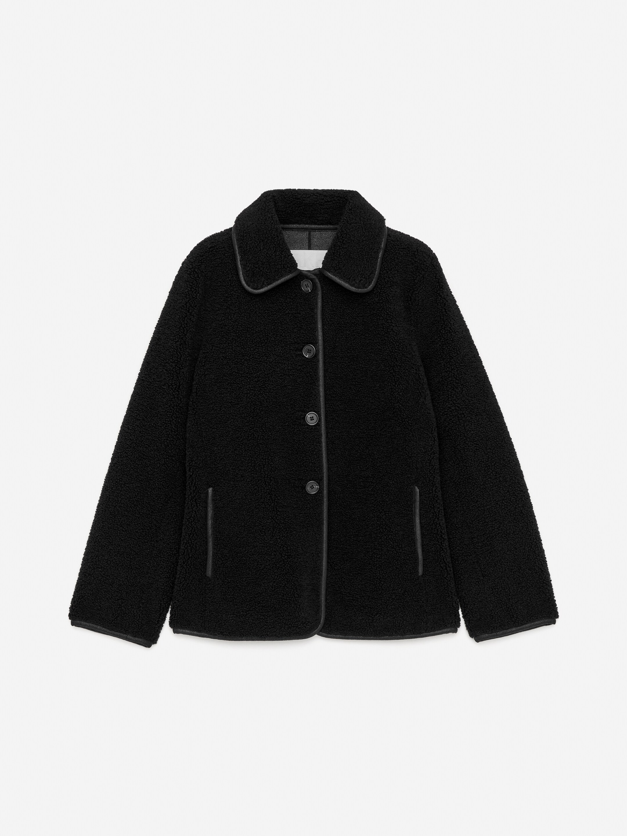 View larger image: A black teddy fleece jacket is shown from the front, featuring a rounded collar and a central button closure. It is detailed with black leather-look piping along the collar, down the front placket, around the hem, and outlining the two vertical slit pockets.