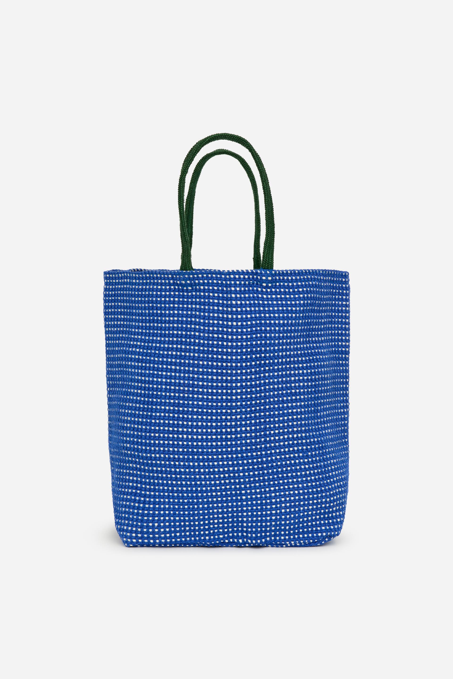 Agrandir l'image: Un sac cabas à l'avant présente un corps tissé bleu avec un motif à carreaux blancs et deux poignées en corde vert foncé.