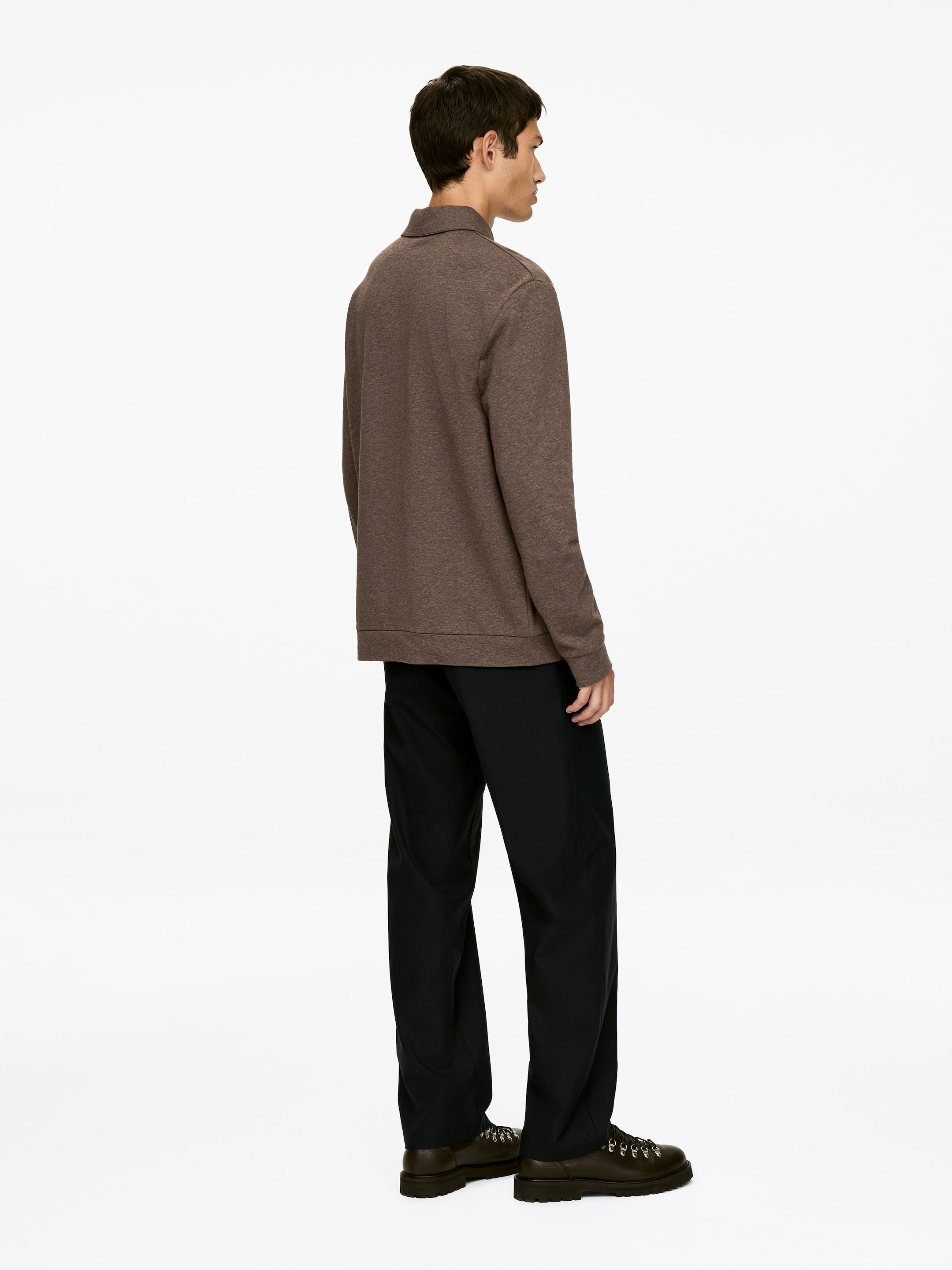 Grotere afbeelding bekijken: Een bruine polo met lange mouwen wordt vanuit een zijaanzicht gepresenteerd. Het heeft een gestructureerde kraag en vertoont een gebreide stof met textuur. Het shirt wordt gestyled met zwarte relaxed-fit broek en donkere veterschoenen, die zijn voorzien van chunky zolen.