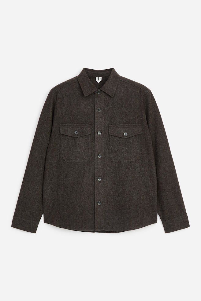 Ein dunkelbraunes, strukturiertes Overshirt aus Wollmischung ist frontal dargestellt und verfügt über einen spitzen Kragen sowie einen zentralen Knopfverschluss mit dunklen Knöpfen. Es zeigt zwei symmetrische aufgesetzte Brusttaschen mit geknöpften Patten, lange Ãrmel und einen geraden Saum. - 1