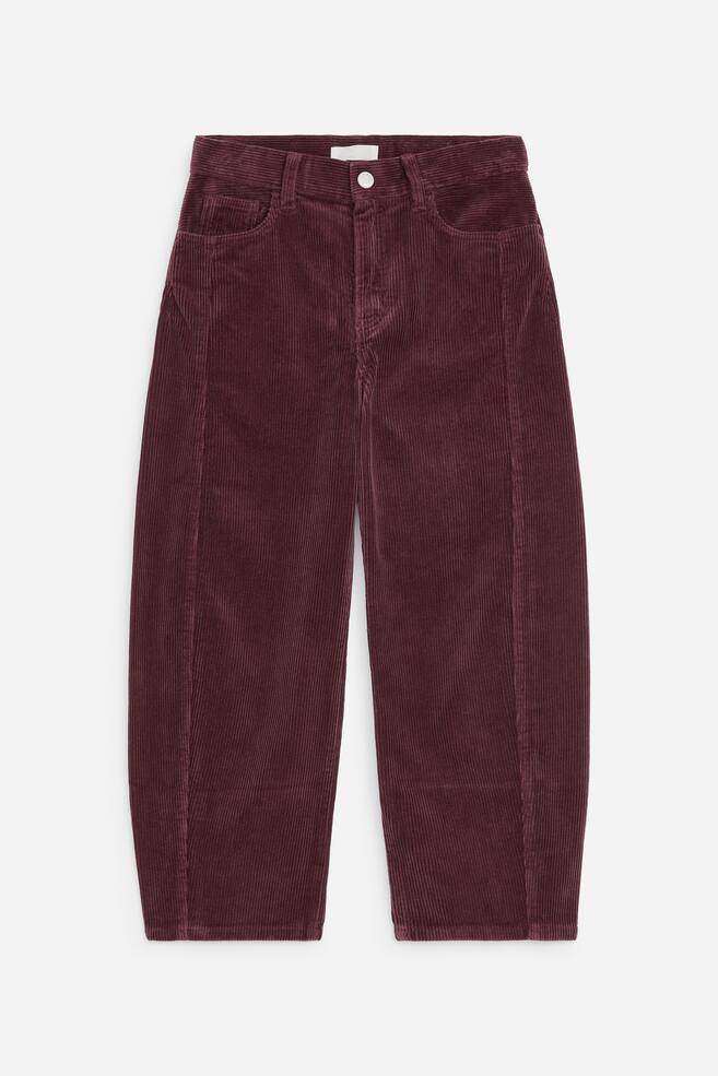 Burgunderfarbene Cordhose von vorne dargestellt, mit hochgeschnittener Barrel-Leg-Silhouette und geschwungenen Ã¤uÃeren Nahtpartien. Das Design umfasst eine klassische Five-Pocket-Konstruktion, GÃ¼rtelschlaufen und einen einzelnen Knopfverschluss am Bund. - 1