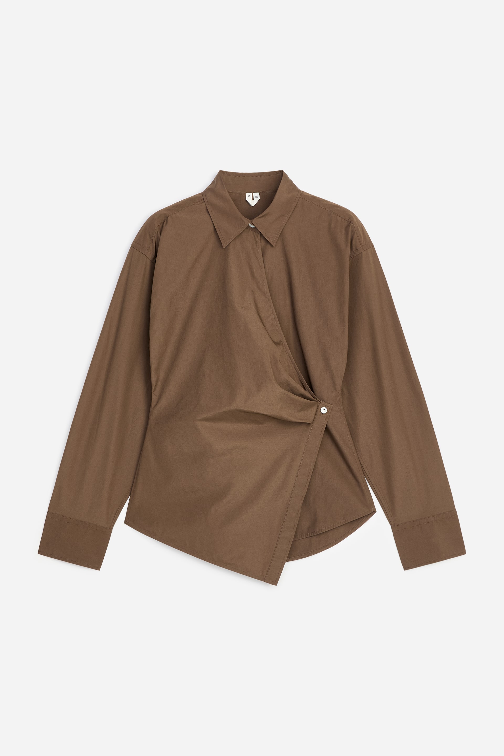 Grotere afbeelding bekijken: Een bruine overslagblouse wordt frontaal gepresenteerd, met een klassieke kraag en lange mouwen met knoopmanchetten. De voorpanden overlappen diagonaal en worden vastgezet met een enkele witte knoop, wat een asymmetrische zoom creëert.