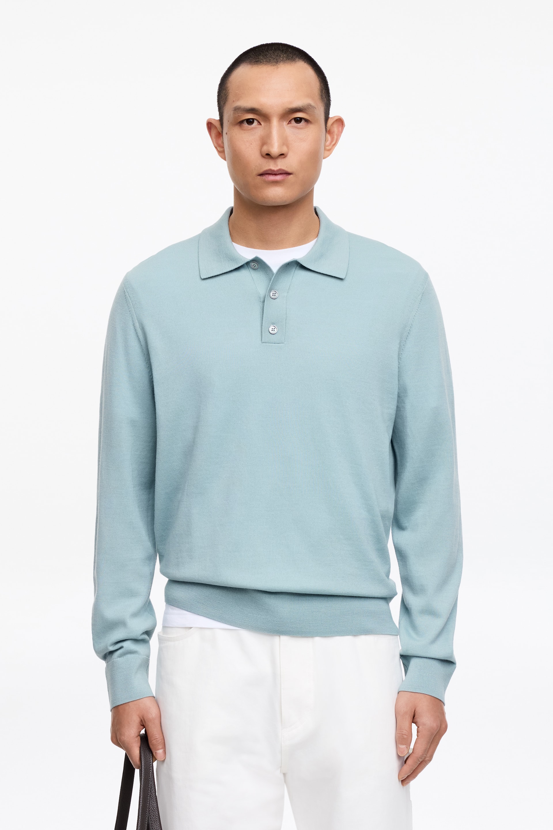 Visa större bild: En ljusblå långärmad stickad polotröja presenteras, med en spetsig krage och en treknappslå. Den har ribbade muddar och en ribbad fåll, och är lagrad över en vit t-shirt.