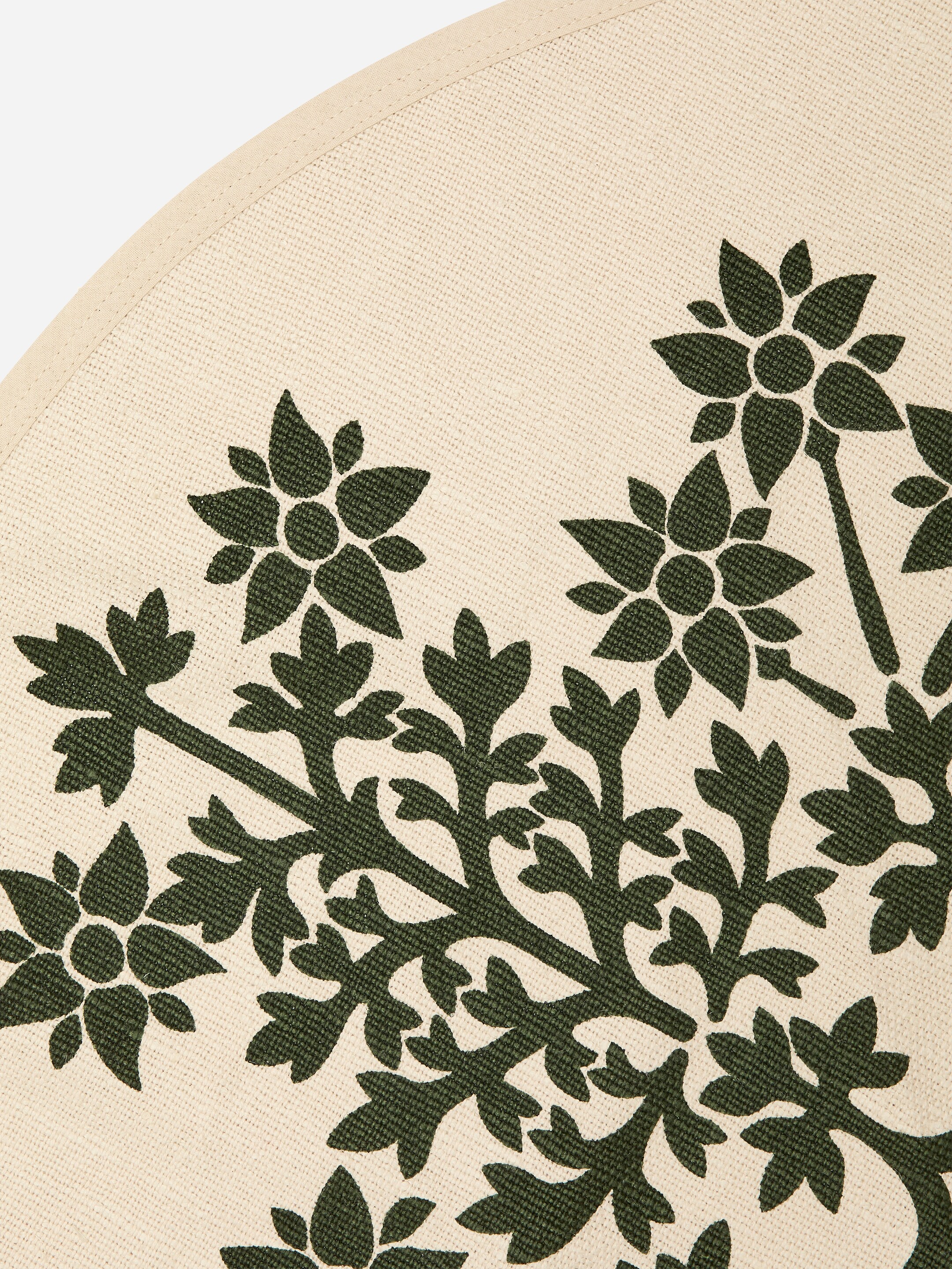 Visa större bild: En rund matta presenterar en väv av krämfärgad yta med ett mörkgrönt botaniskt motiv på dess framsida. Motivet har stiliserade blommor och blad som sprider sig över mattan från botten och centrum.