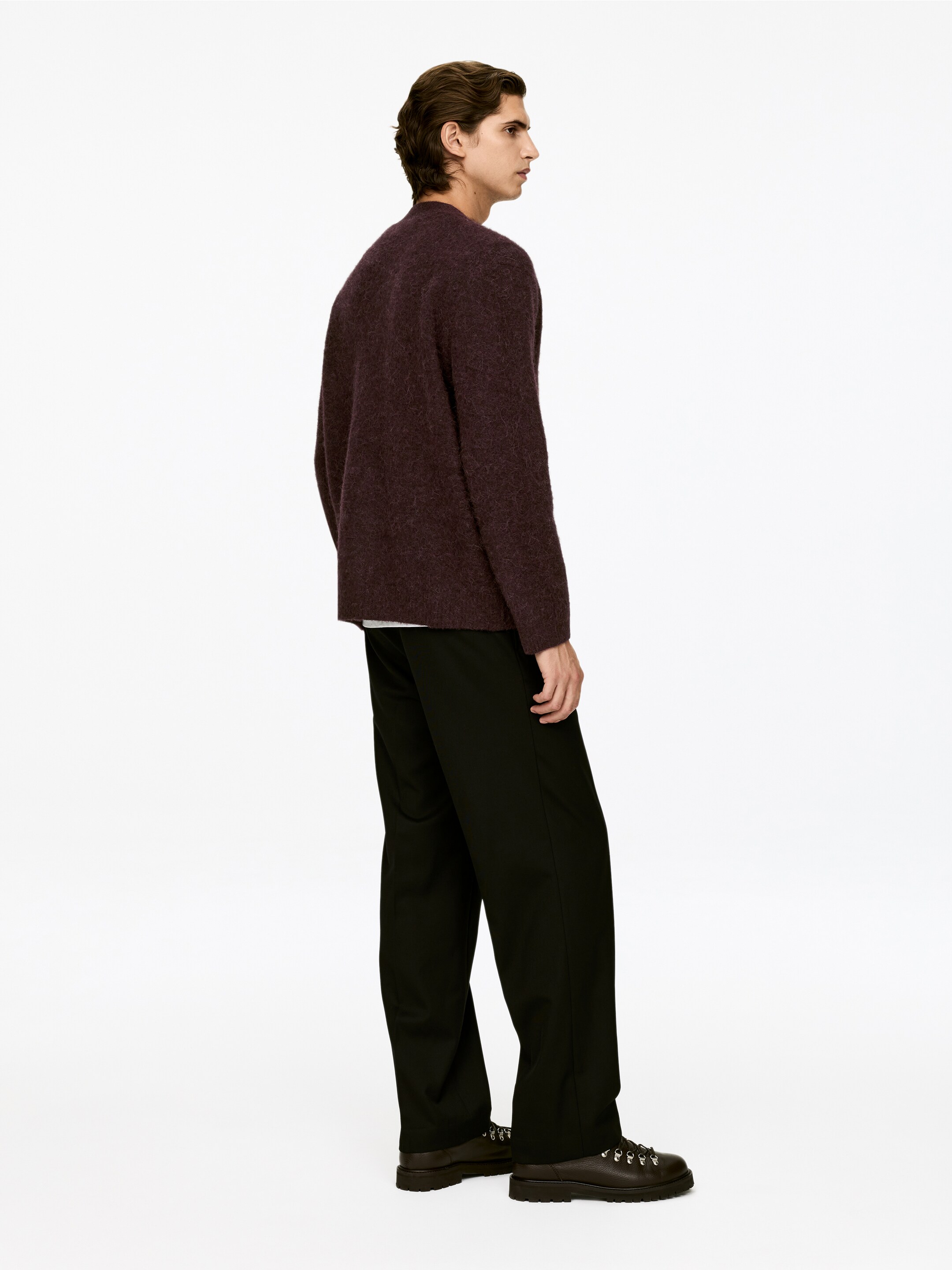 Ver imagem maior: Um camisola de malha roxa escura e felpuda está a ser apresentada de um ângulo lateral-traseiro, apresentando um corte descontraído e mangas compridas, e está sobreposta a uma t-shirt branca. Calças pretas de corte descontraído também estão a ser usadas, estendendo-se até aos tornozelos e emparelhando com botas de atacadores castanhas escuras.