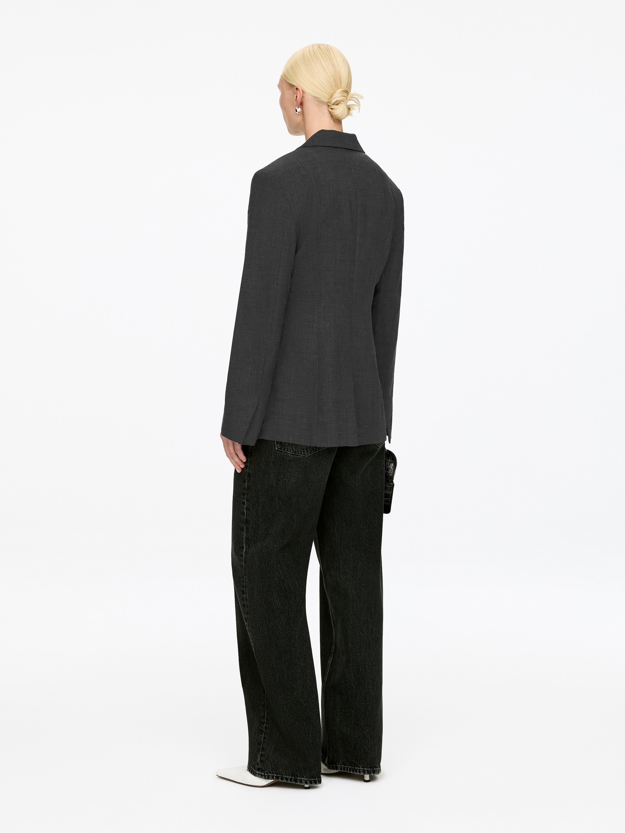 Visa större bild: En mörkgrå blazer visas från baksidan, med en skräddarsydd silhuett och långa ärmar. Den bärs över svarta jeans med vida ben.
