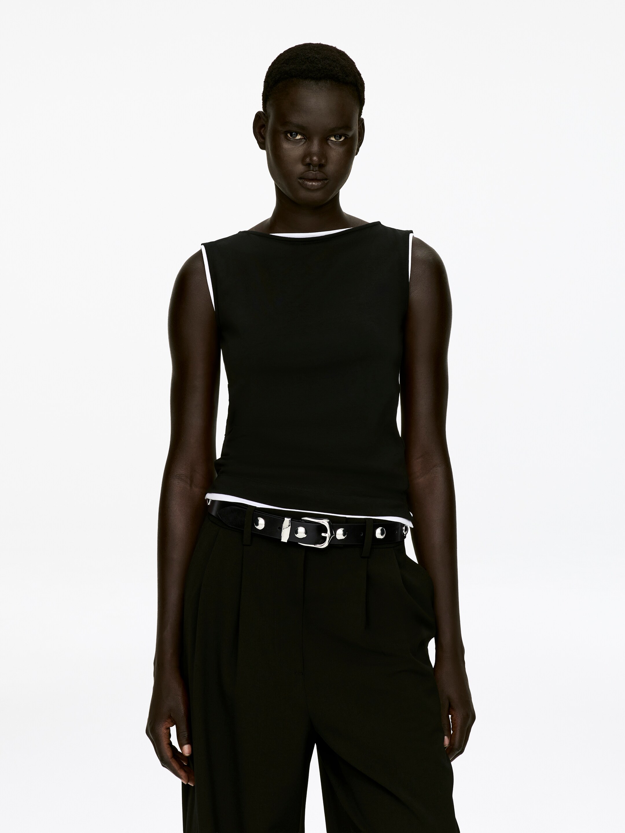 Ver imagen más grande: Un cinturón de cuero negro con tachuelas está siendo usado por la modelo, posicionado en las caderas. El cinturón cuenta con tachuelas circulares de tono plateado y una hebilla rectangular, ajustando unos pantalones negros.
