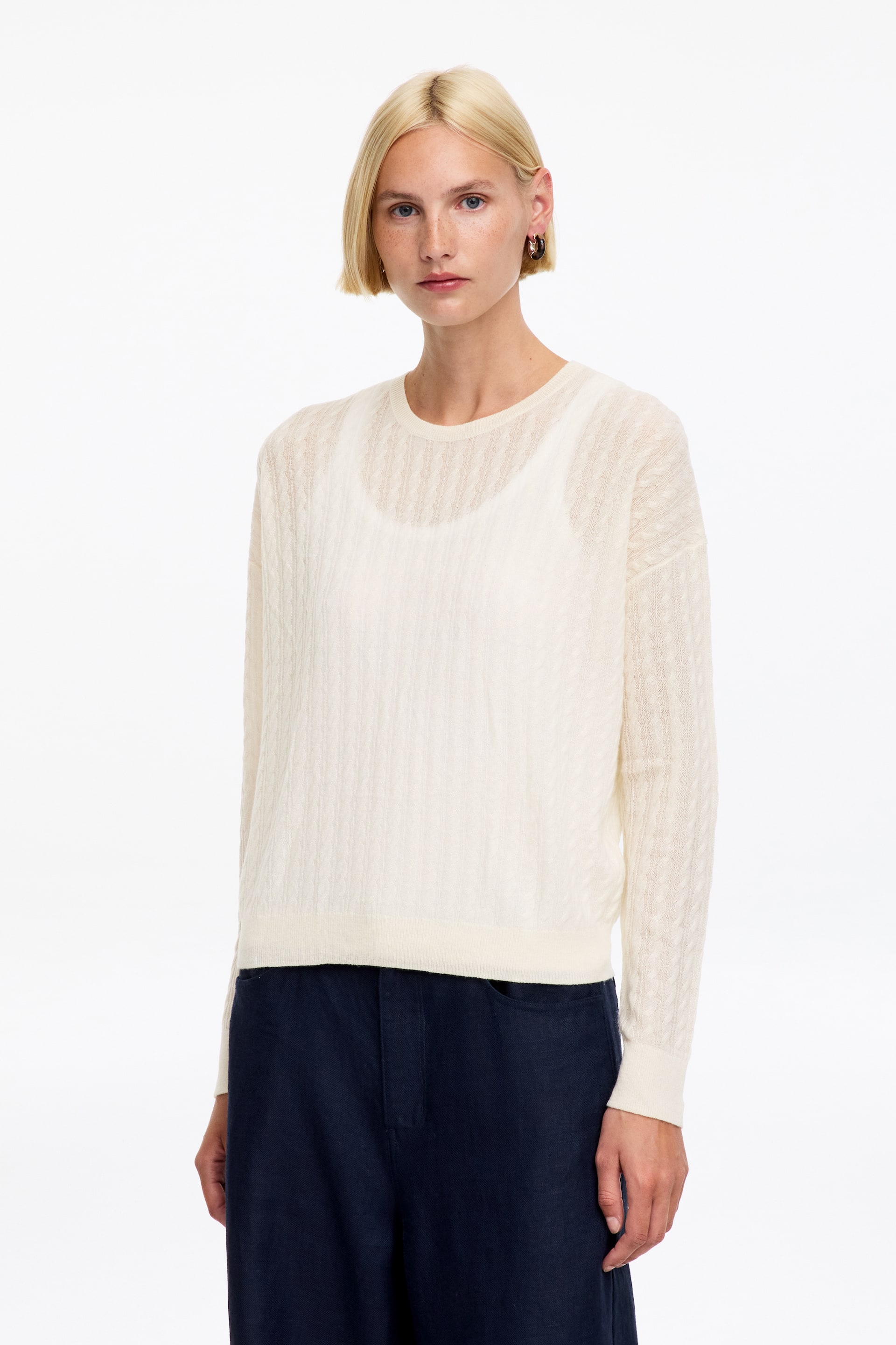 Ver imagem maior: Um camisola de gola redonda de cor creme, com um padrão de malha texturada delicada ao longo do corpo e das mangas compridas. Apresenta punhos e bainha canelados, com uma camisola interior branca visível por baixo.