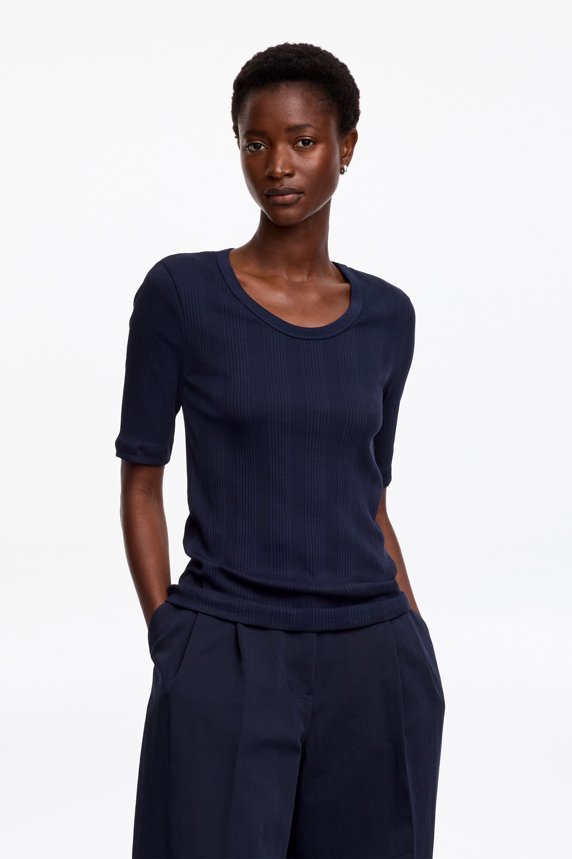 Visualizza l'immagine ingrandita: Un top a maniche corte in maglia a coste blu navy presenta uno scollo tondo e un orlo a coste. Viene presentato insieme a pantaloni plissettati blu navy coordinati con tasche laterali visibili, con entrambi i prodotti rivolti in avanti.
