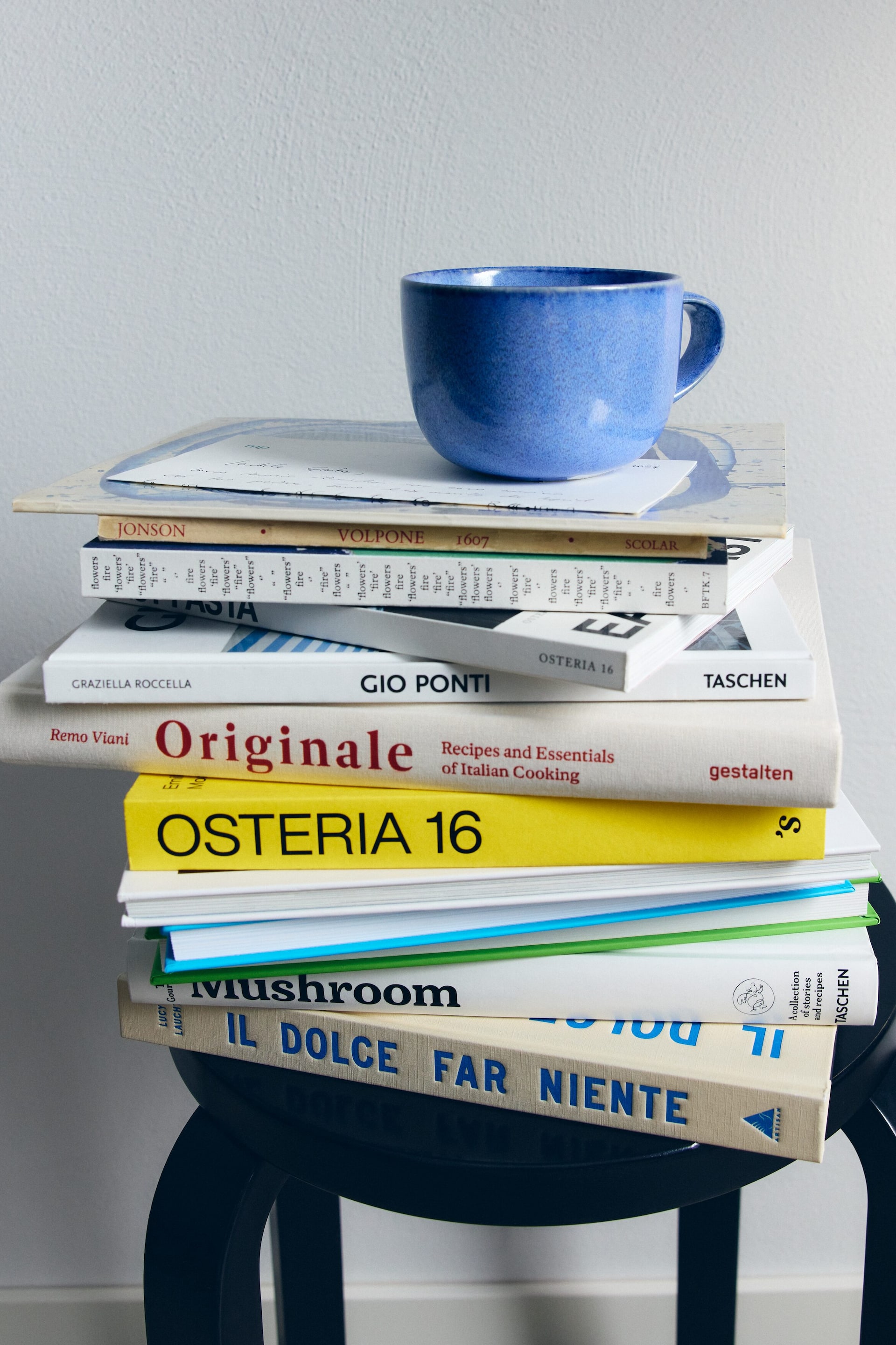 Visualizza immagine più grande: Una tazza in ceramica blu è appoggiata su una pila di libri, con finitura puntinata e corpo arrotondato. Il manico a forma di C è visibile sul lato destro, mentre la tazza è orientata leggermente verso sinistra.