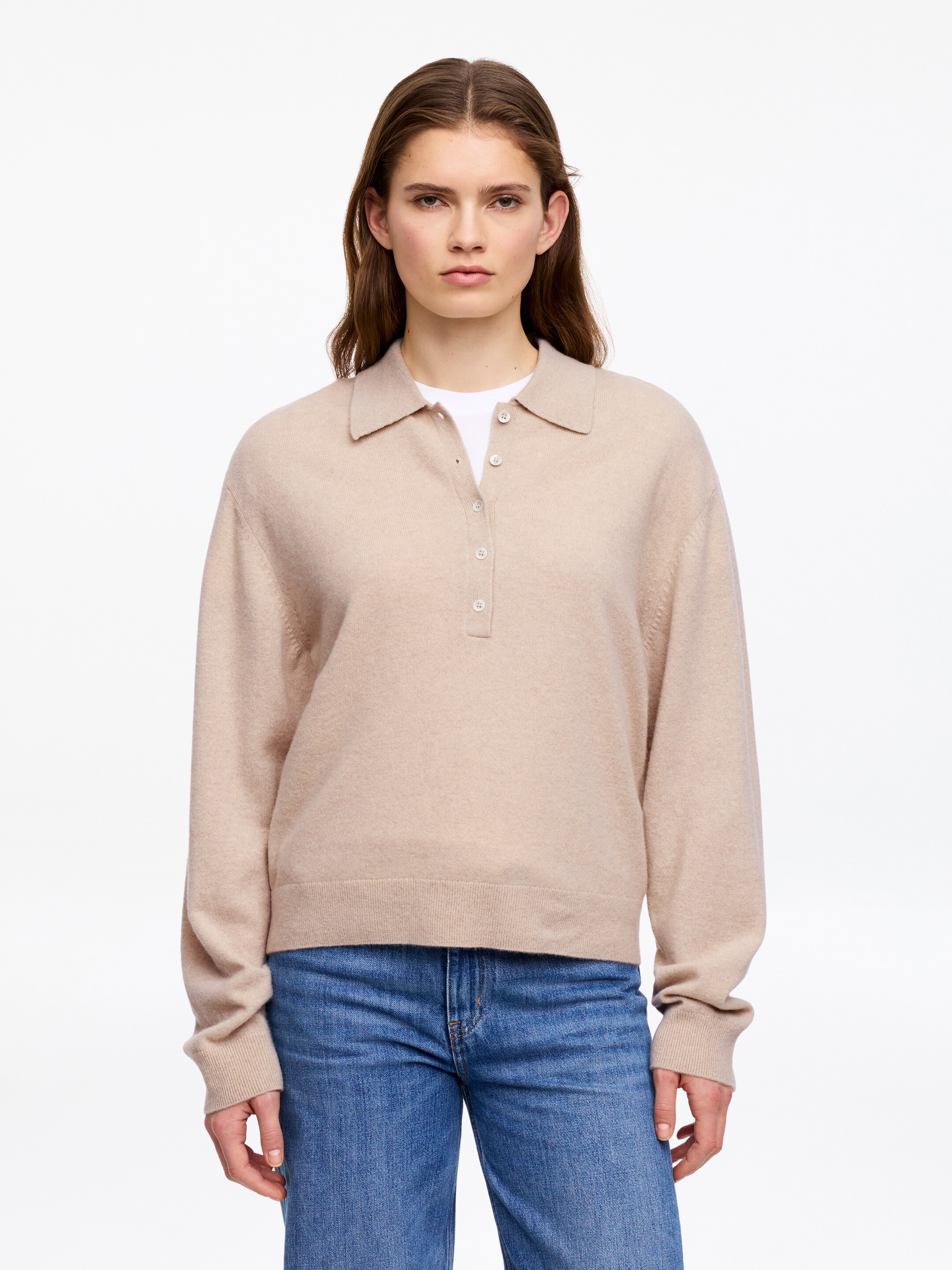 Grösseres Bild ansehen: Ein beige Polo-Pullover mit einem Kragen und einer Vier-Knopf-Leiste, darunter ist ein weißes Unterhemd sichtbar. Der Pullover ist mit langen Ärmeln, gerippten Bündchen und einem gerippten Saum gestaltet.