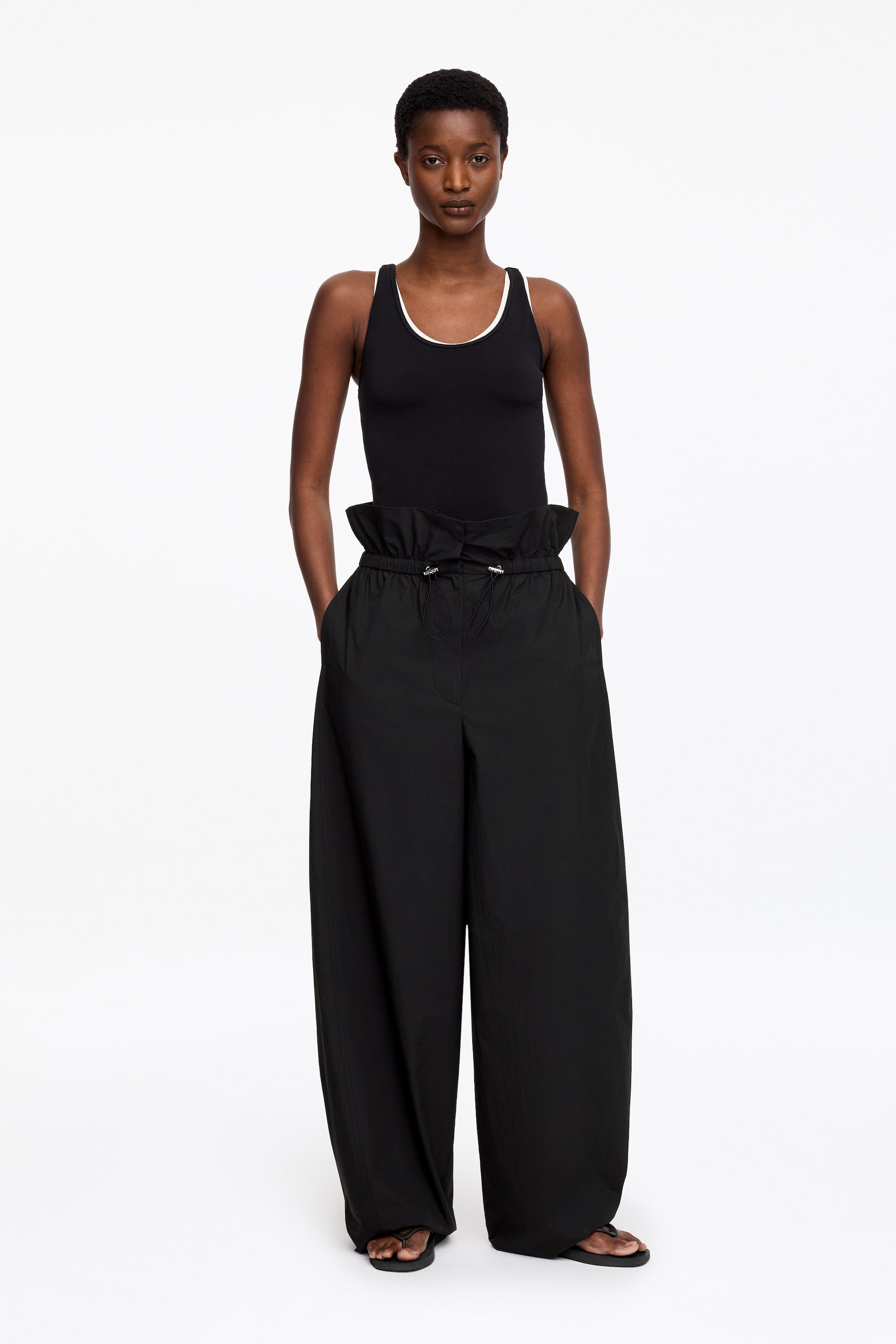 View larger image: A black vest top, which features white trim at the neckline and armholes, is being worn, facing forward. It is paired with black wide-leg trousers that boast a high, cinched paper-bag waist with drawstring details, side pockets, and a relaxed, flowing fit.
