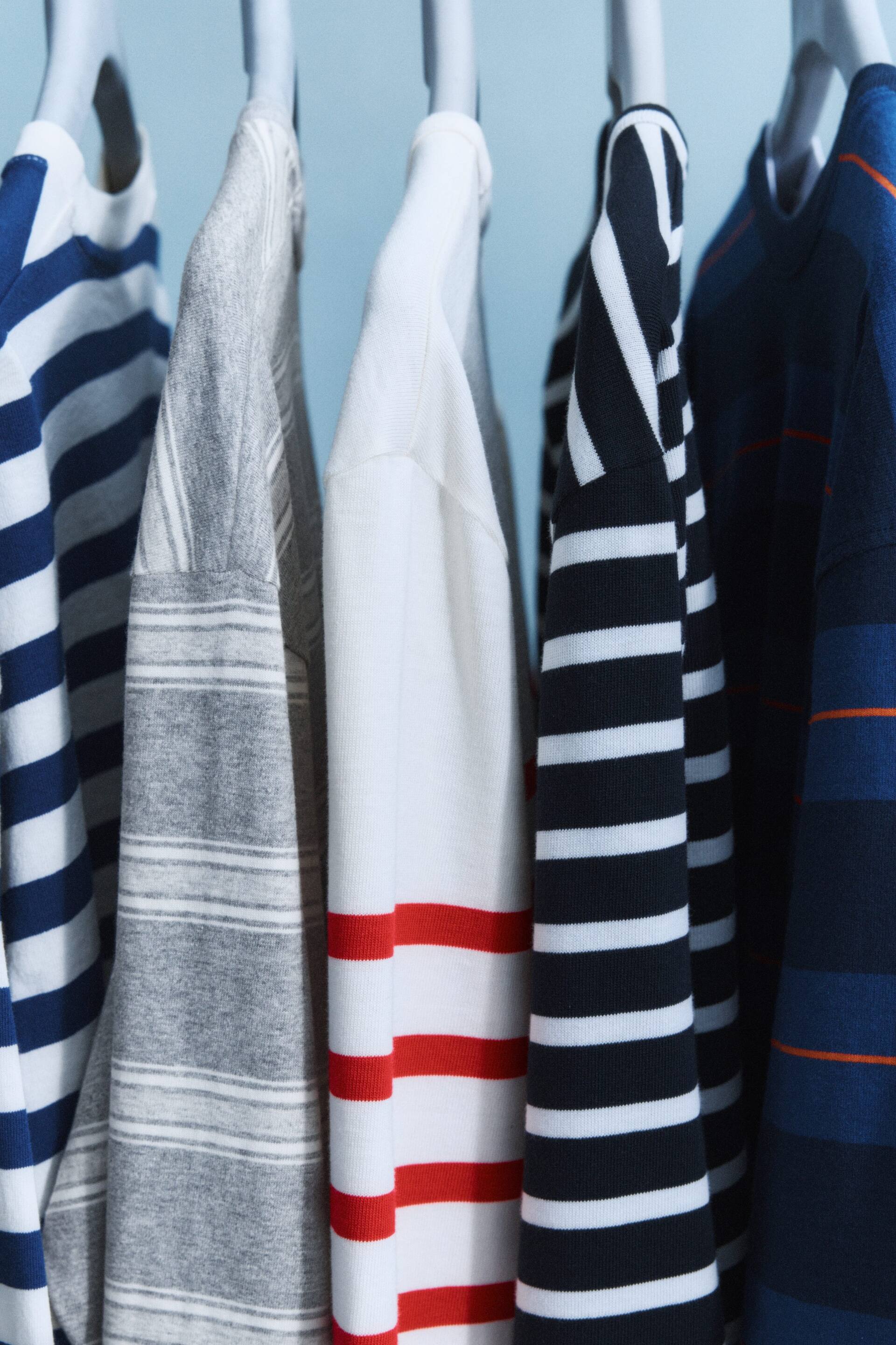 Visualizza immagine più grande: Le camicie a righe sono appese, caratterizzate da vari motivi a righe orizzontali. I colori includono blu navy e bianco, grigio e bianco, rosso e bianco, nero e bianco, e blu scuro con righe di accento arancione.