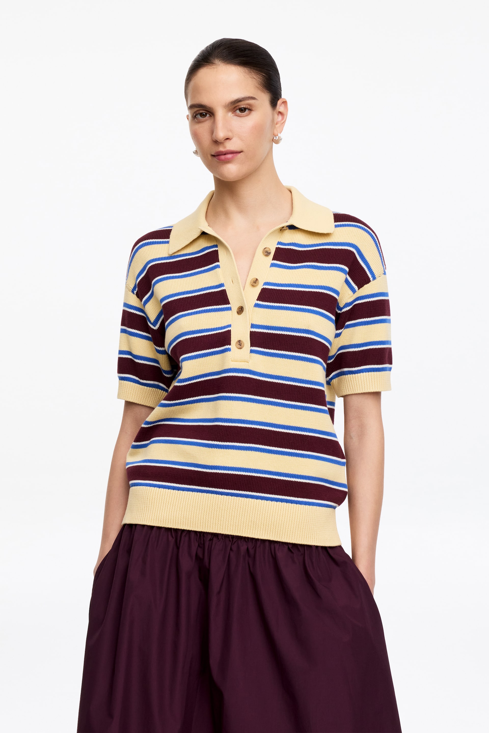 Größeres Bild anzeigen: Ein Poloshirt mit horizontalen Streifen in Gelb, Burgund, Blau und Weiß, die nach vorne zeigen. Es ist mit einem gelben Polokragen, einer Dreiknopfleiste mit hellbraunen Knöpfen, kurzen Ärmeln und einem gerippten Saum gestaltet.