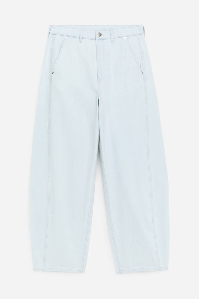 FRENTE: Calças de ganga em forma de barril, de cor azul claro, apresentam um estilo de cintura média com bolsos laterais inclinados e rebites de metal. Um fecho de correr com um único botão está presente na cintura, e detalhes de costura vertical percorrem a frente de cada perna. - 1