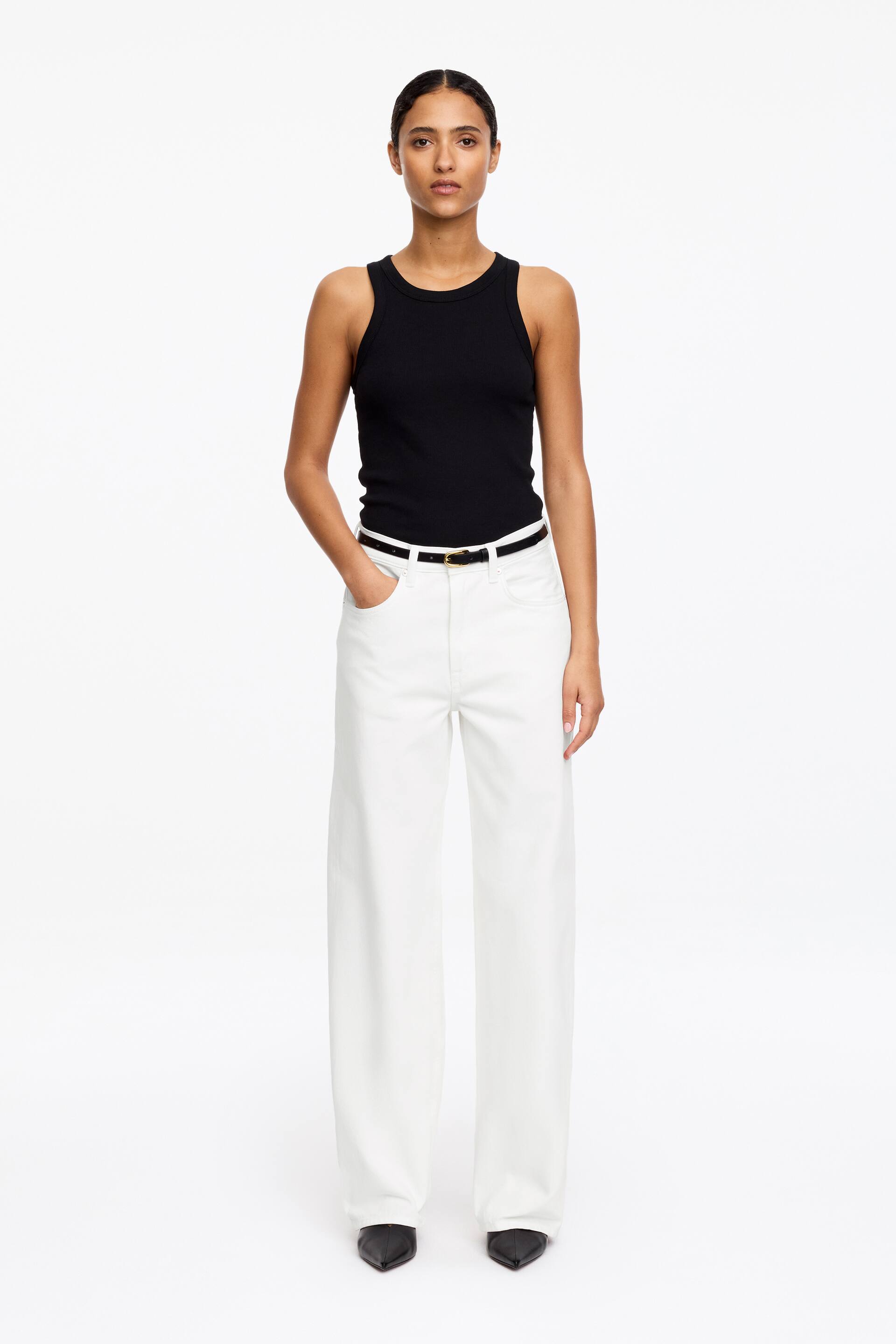Agrandir l'image: Un débardeur côtelé noir est présenté de face, montrant un col rond et des épaules sans manches. Il épouse étroitement le corps et est rentré dans un pantalon blanc.