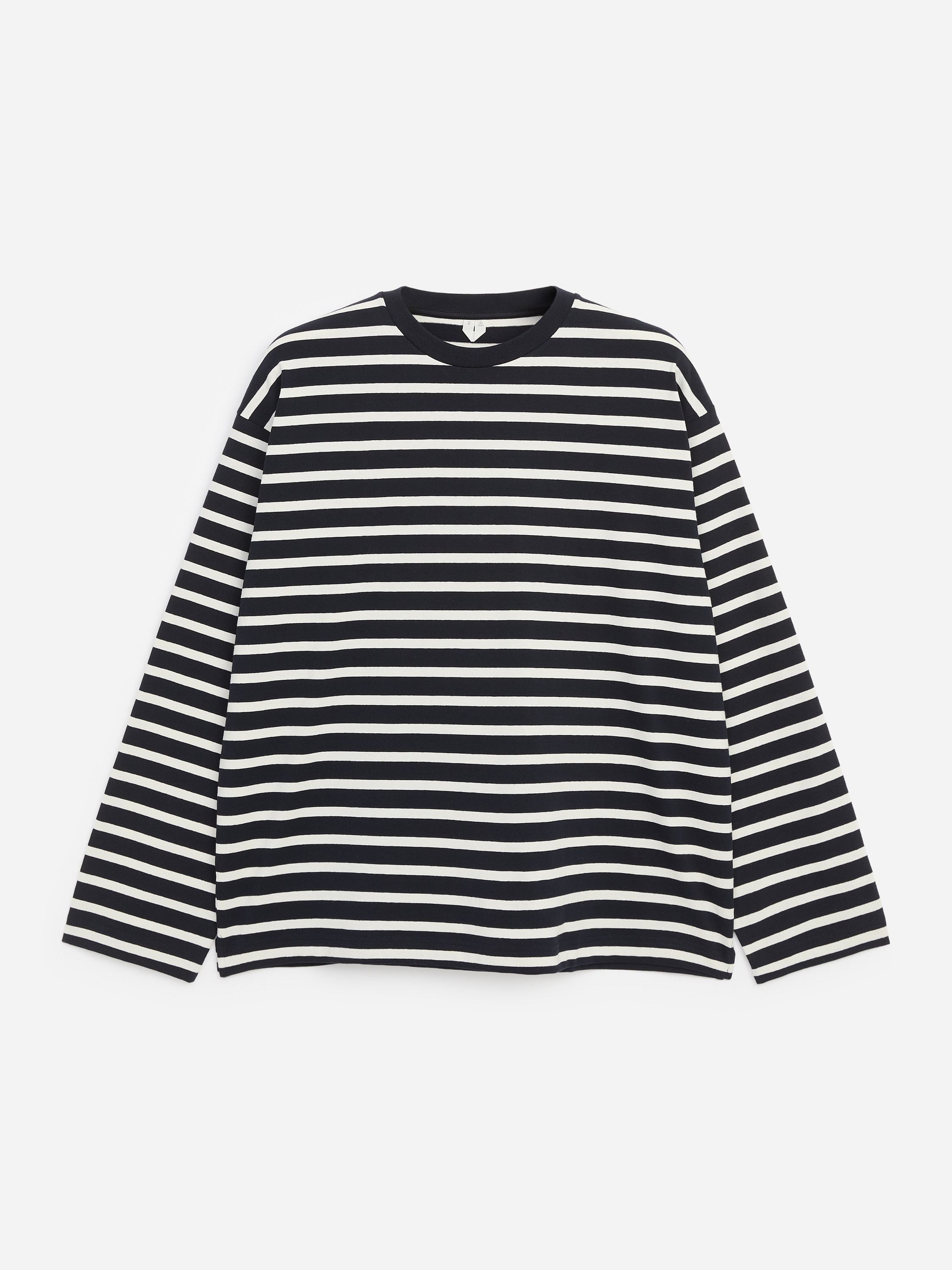 En T-shirt med afslappet pasform, lange ærmer og rund hals med sorte og hvide vandrette striber bæres af modellen. Modellen kombinerer T-shirten med blå jeans, mens hun står og vender fronten mod kameraet.