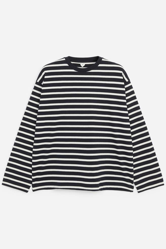 Un T-shirt Ã  manches longues coupe dÃ©contractÃ©e, Ã  rayures horizontales noires et blanches, est posÃ© Ã  plat, vu de face. Le vÃªtement prÃ©sente un col rond cÃ´telÃ© uni de couleur foncÃ©e, des Ã©paules tombantes et des manches larges Ã  coupe droite. - 1