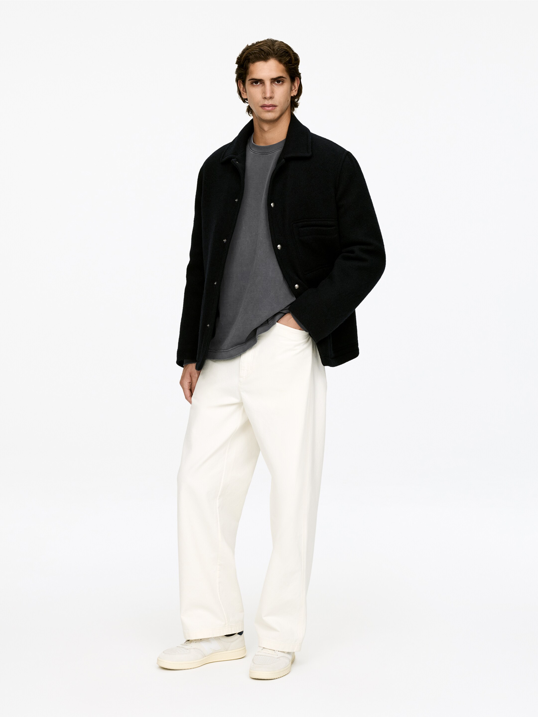View larger image: A black textured jacket is being worn open over a gray round-neck t-shirt, while cream-colored wide-leg pants are being worn, falling to the ankles. The jacket is displaying a collar, long sleeves, front snap closures, and a visible chest pocket, with all items presented from a front-facing, slightly angled perspective.