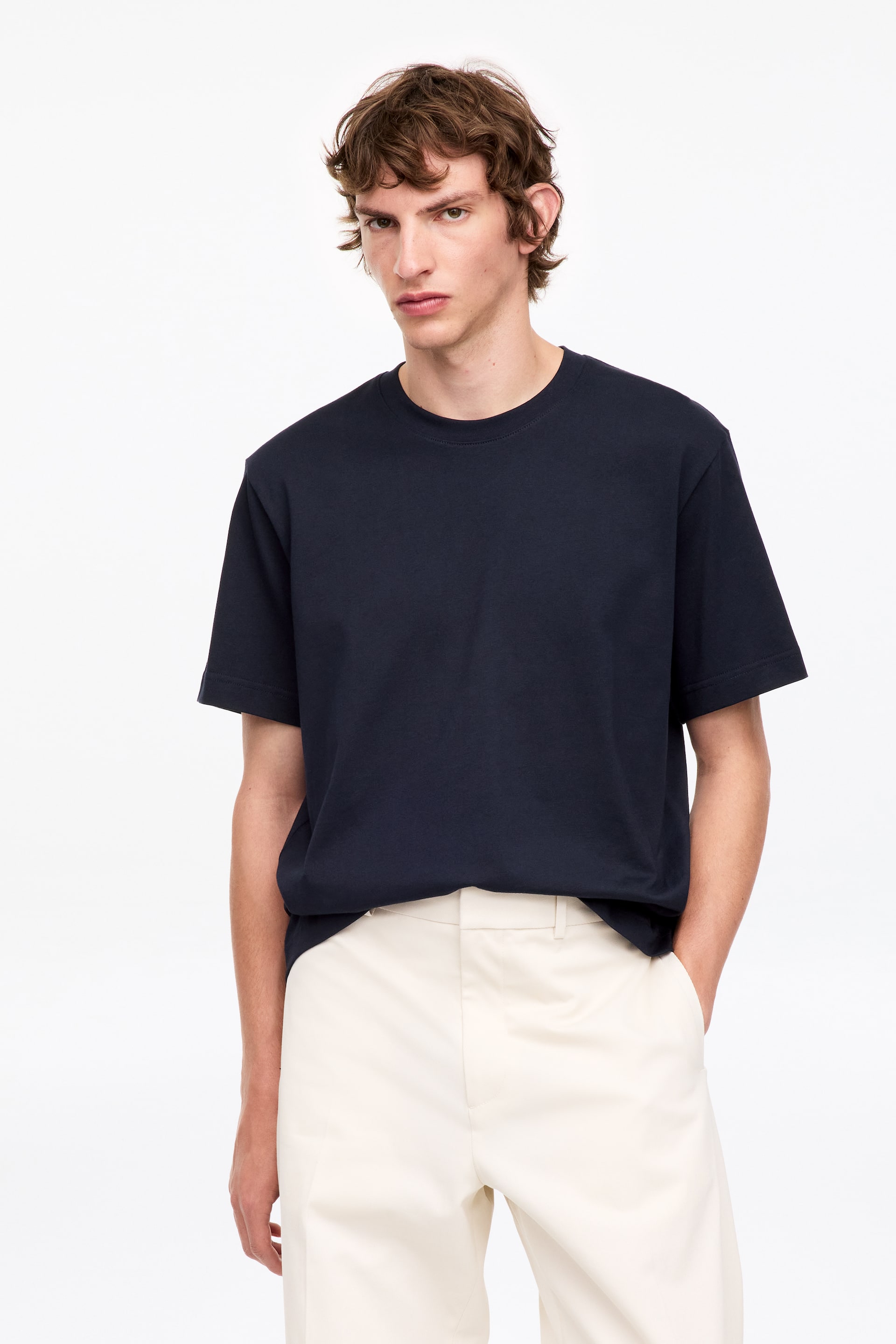 Se større billede: En mørkeblå t-shirt præsenteres forfra, med rund halsudskæring og korte ærmer, og har en afslappet pasform, hvor stoffet falder løst.