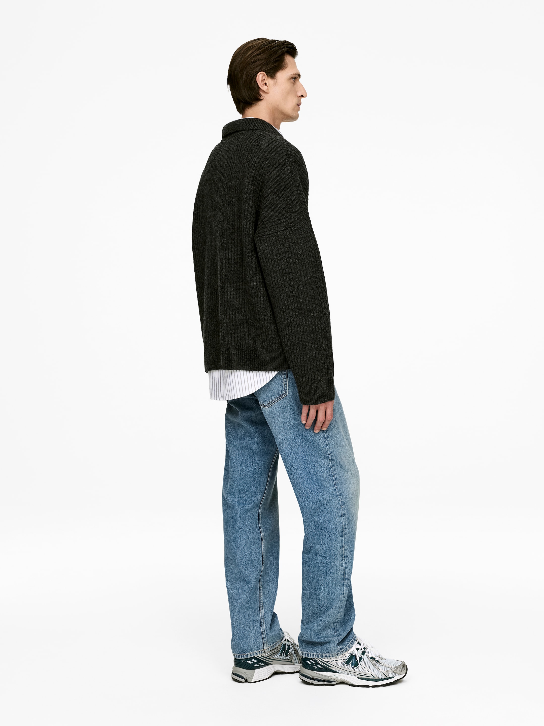 Grotere afbeelding bekijken: Licht gewassen blauwe jeans worden gedragen door het model, met een losse pasvorm, een middelhoog taille en rechte, volledige lengtes pijpen. Een donker geribd trui wordt over de jeans gelaagd en atletische sneakers maken de look compleet.