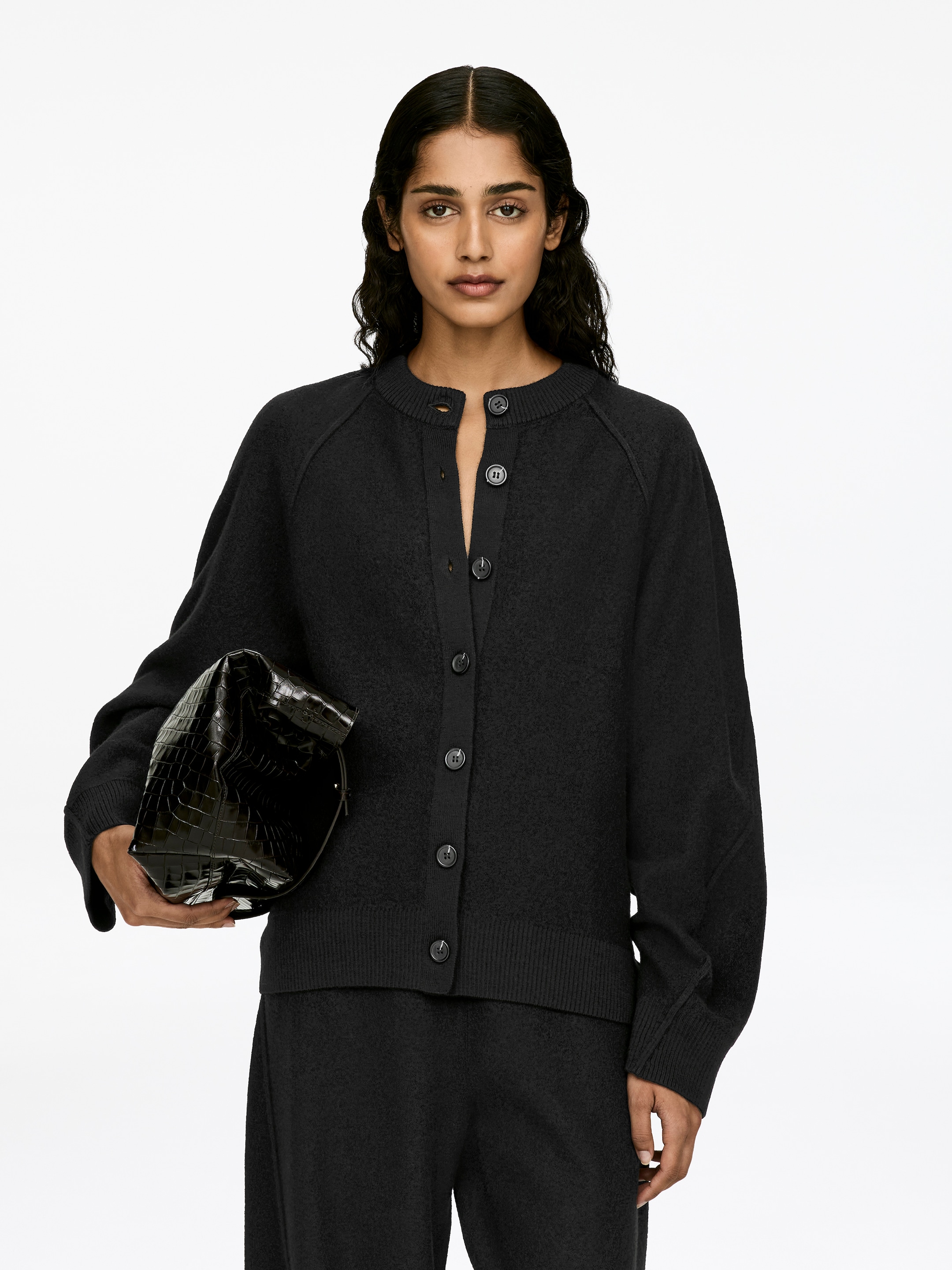 Agrandir l'image: Un cardigan en laine bouillie gris foncé, avec une fermeture à boutons, des bordures côtelées et une coupe ample, est porté par le mannequin. Plusieurs boutons sont défaits, et le cardigan présente des manches raglan et une finition texturée.