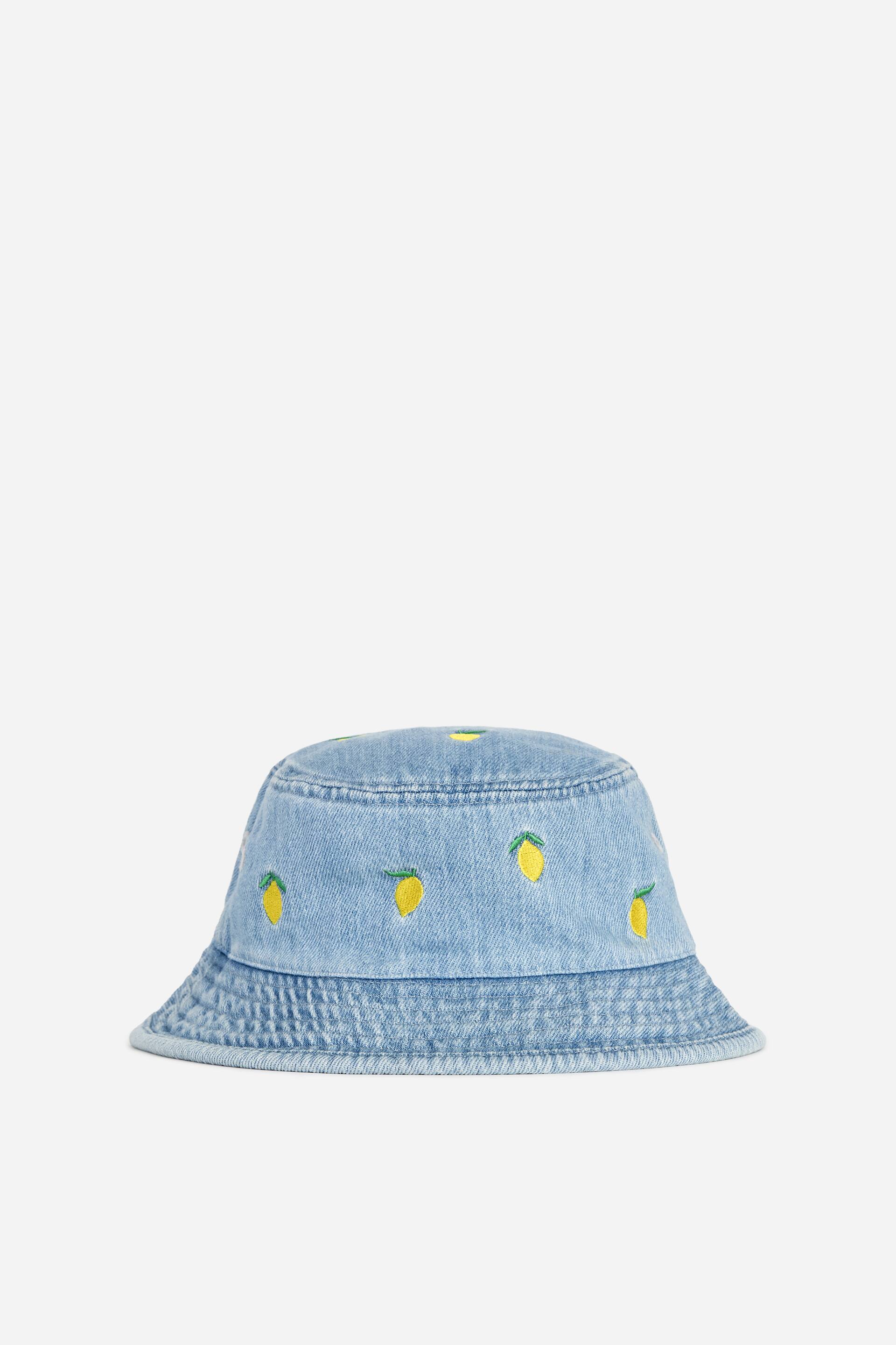 Grotere afbeelding bekijken: Een denim vissershoed toont zijn voorkant, gemaakt van een lichtblauwe katoenen weefsel. Het is versierd met geborduurde gele citroenpatronen met groene stelen over de kroon en de halflange rand.